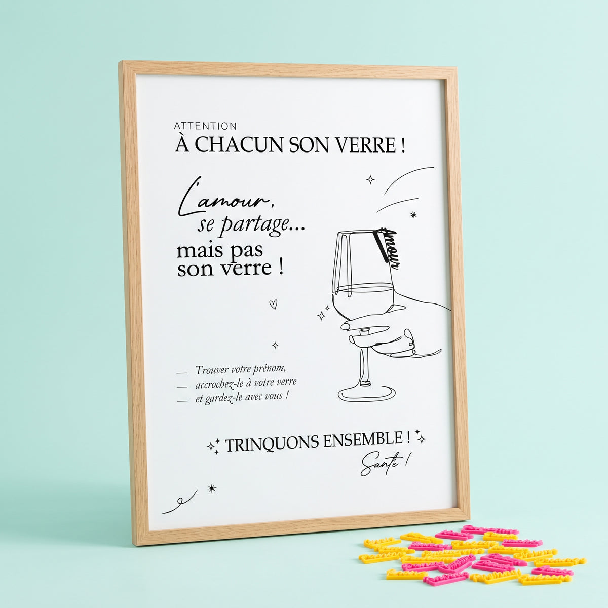 Affiche A3 en cadre bois clair, affichant les messages « À chacun son verre ! », « L'amour, se partage… mais pas son verre ! » et « Trinquons ensemble ! », avec une illustration au trait d'une main tenant un verre à pied. Au premier plan, de petits marque-verres personnalisés sont posés à plat.