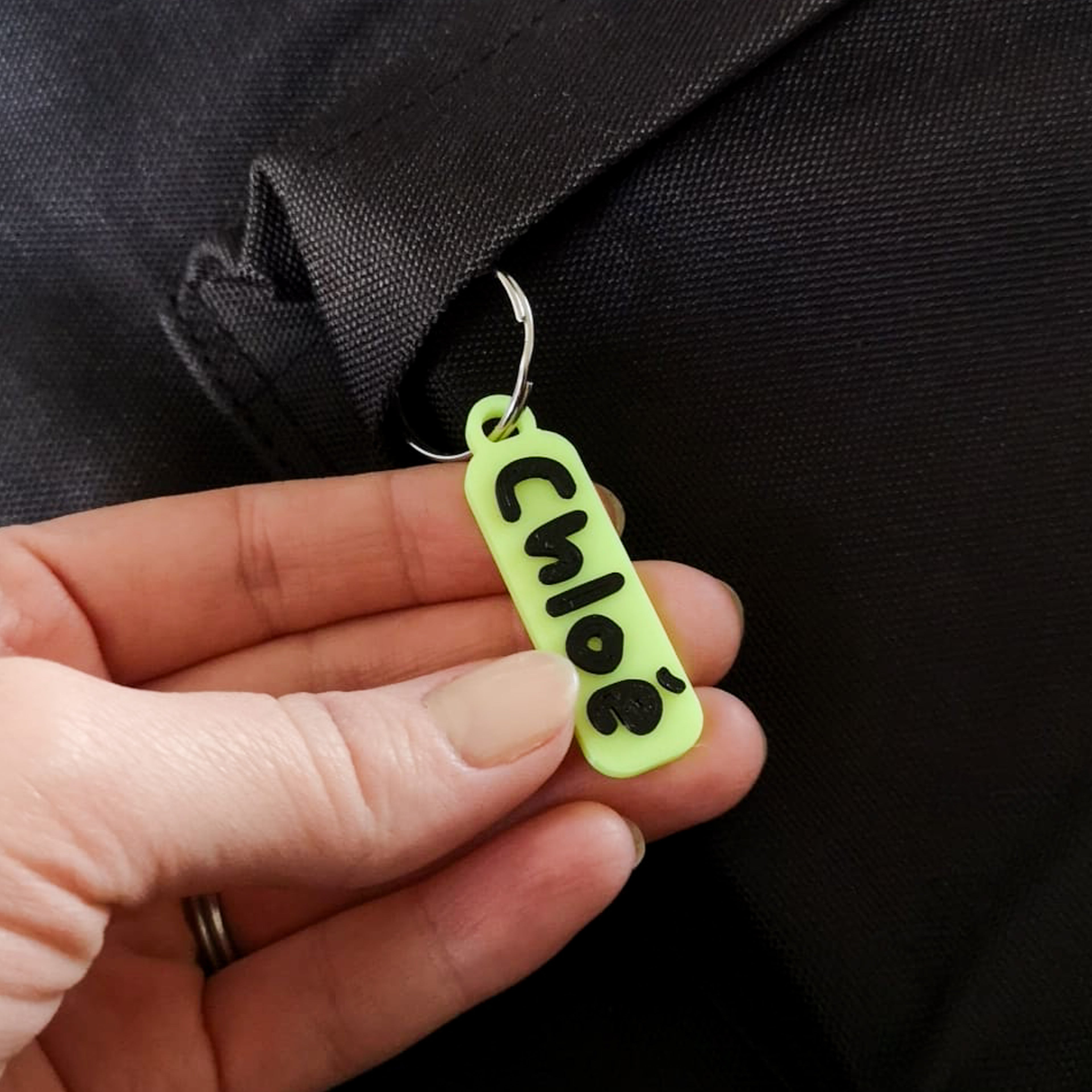 Étiquette 3D prénom « Chloé » en PLA jaune fluo avec lettres noires, montée sur anneau métal, accrochée à un sac.