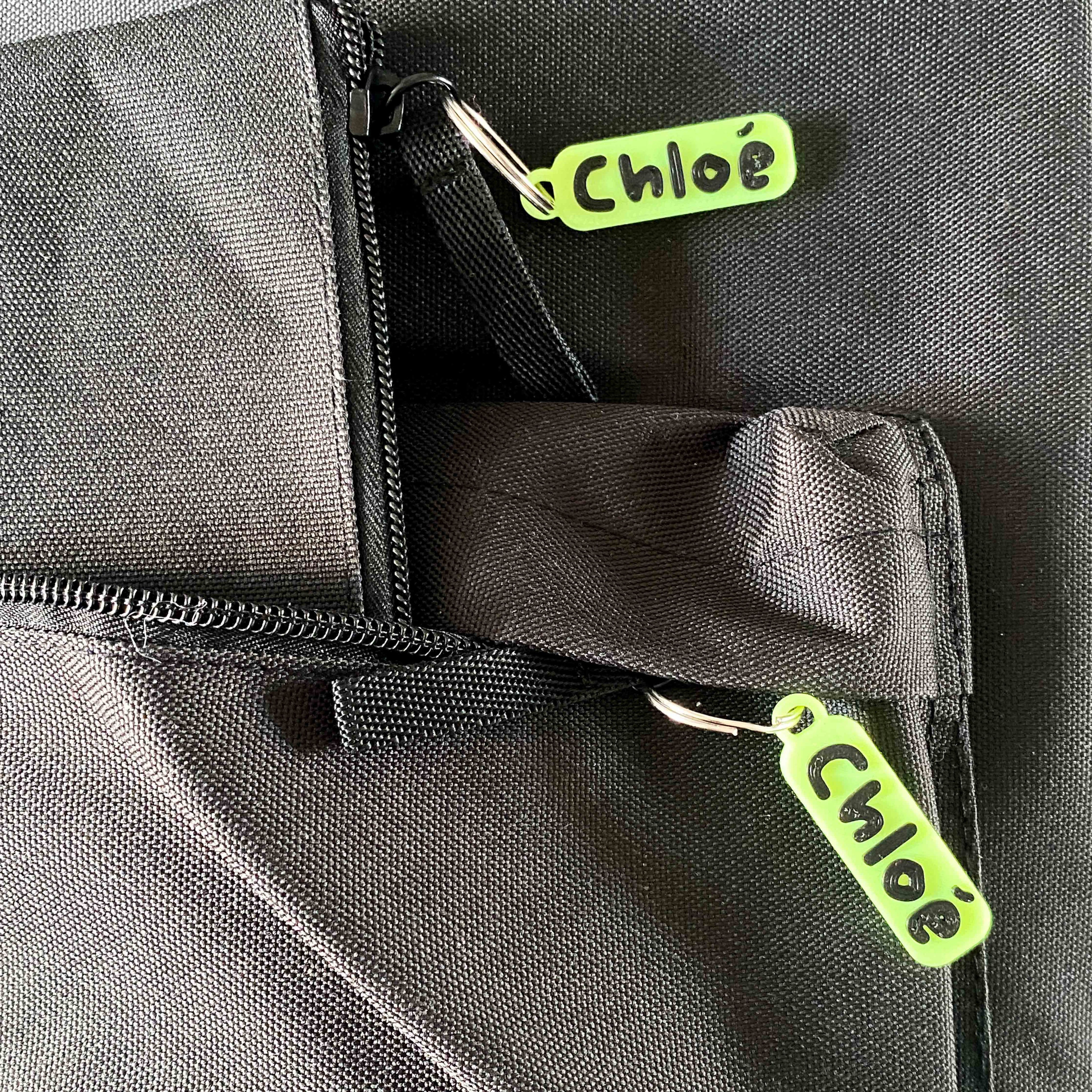 Étiquettes 3D prénom « Chloé » en PLA jaune fluo et noir, accrochées aux fermetures éclair d’un sac et d'une trousse.