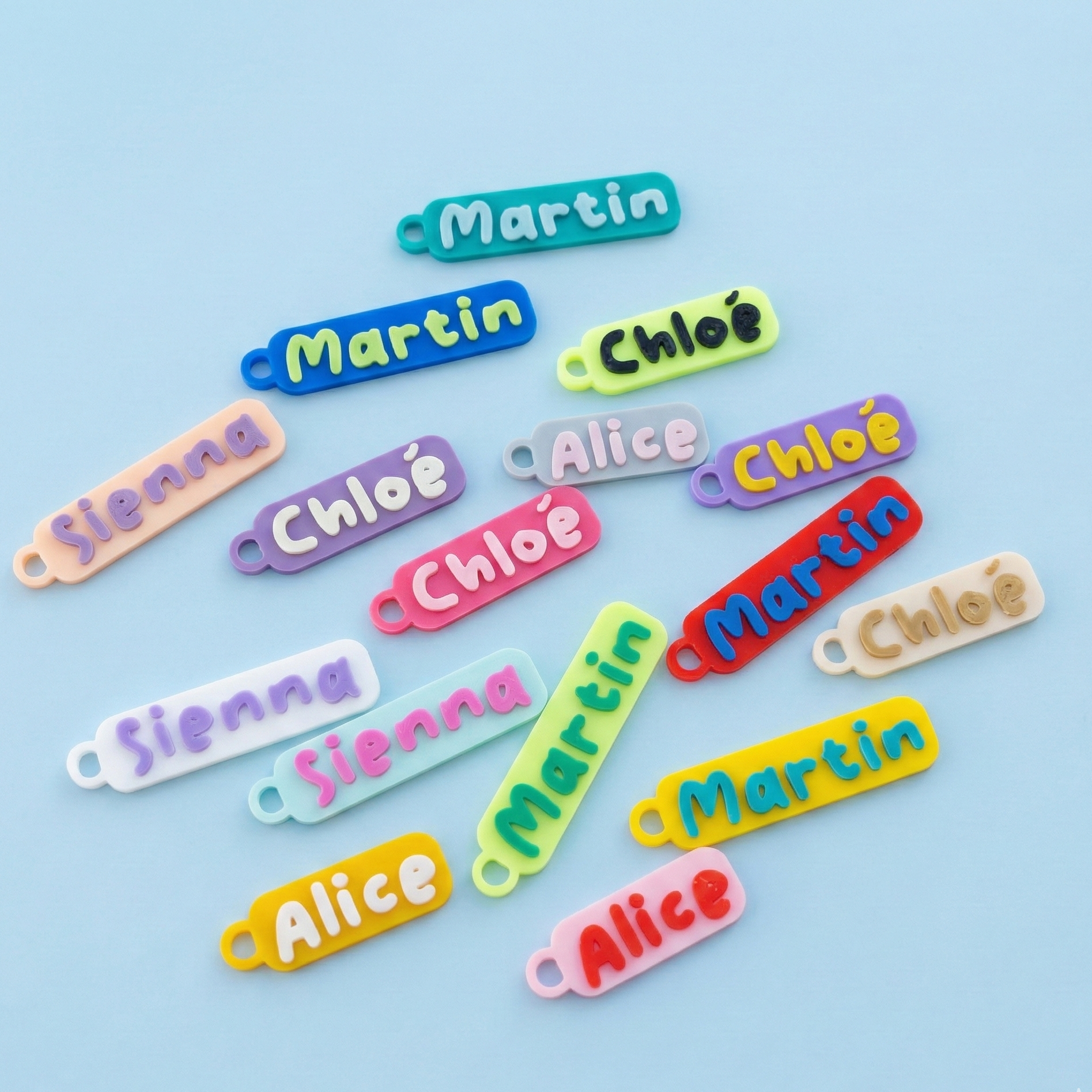 Lot d’étiquettes 3D personnalisées en PLA, bicolores, avec prénoms (Martin, Chloé, Alice, Sienna) sur fond bleu.