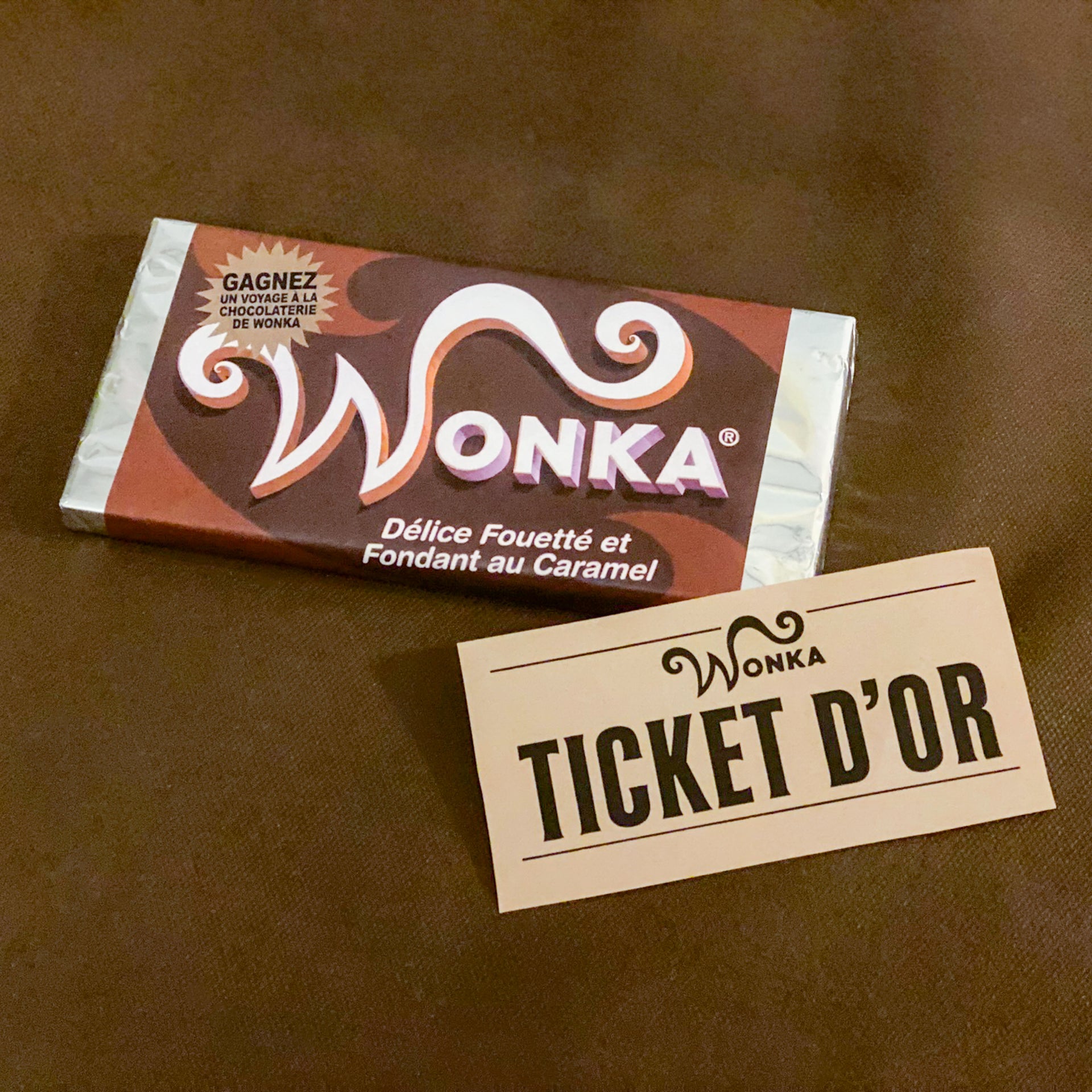 Gros plan sur une tablette de chocolat avec un emballage personnalisé "Wonka" et son célèbre "Ticket d'Or" imprimable. Ces éléments, issus du kit de décoration PDF, permettent de recréer l'univers de Charlie et la Chocolaterie pour un goûter d'anniversaire.