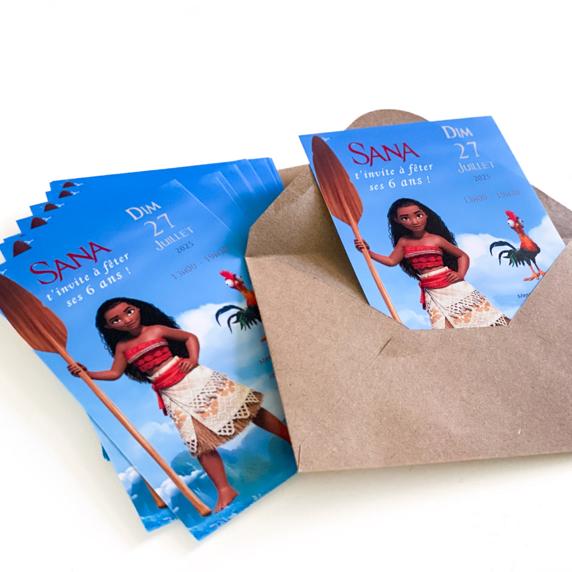 Photo d’invitations imprimées thème Vaiana (Moana) : héroïne polynésienne avec pagaie sur fond océan/nuages, coq Hei Hei à droite, texte « SANA t’invite à fêter ses 6 ans – Dim 27 juillet 2025 – 13h00–19h00 », cartes empilées avec enveloppe kraft.