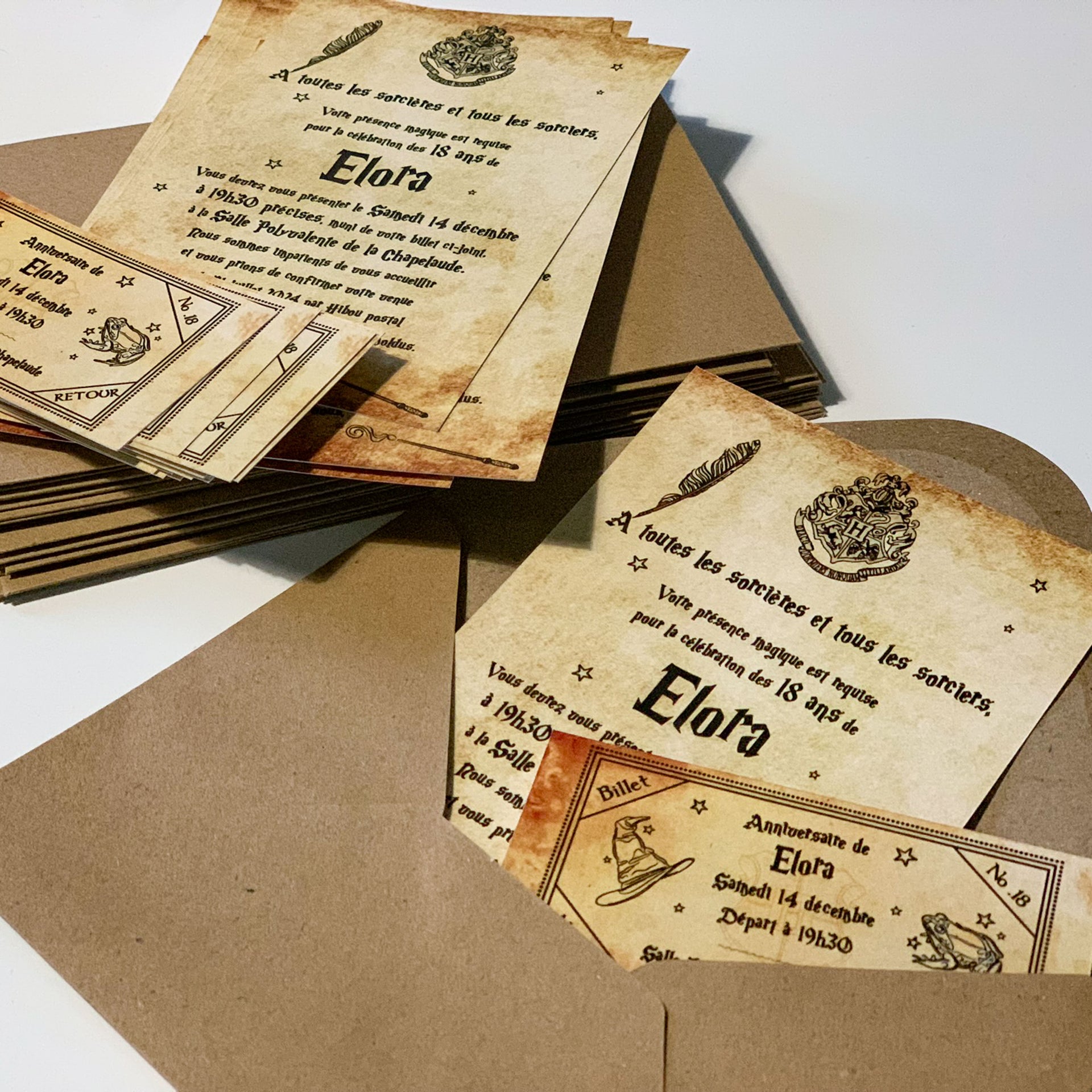 Photo d’invitations imprimées style parchemin vintage pour anniversaire “Harry Potter” : texte noir décoré d’une plume, d’un blason magique, billets façon ticket de train, cartes A6 posées avec enveloppes kraft.
