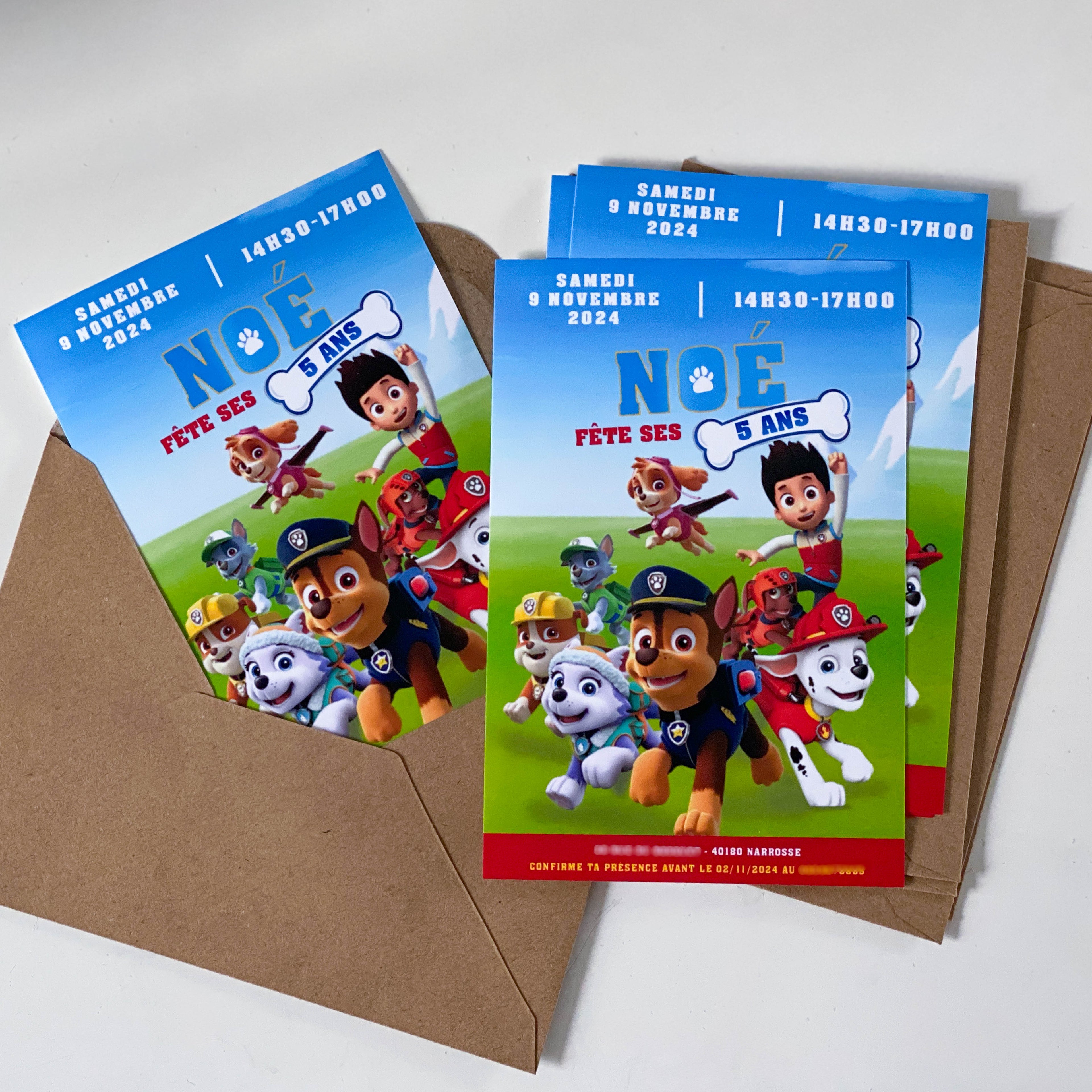 Photo de plusieurs invitations imprimées A6 pour anniversaire enfant, thème Pat'Patrouille : fond ciel/colline, texte « NOÉ fête ses 5 ans » (os blanc), samedi 9 novembre 2024 – 14h30–17h00, cartes posées dans une enveloppe kraft.