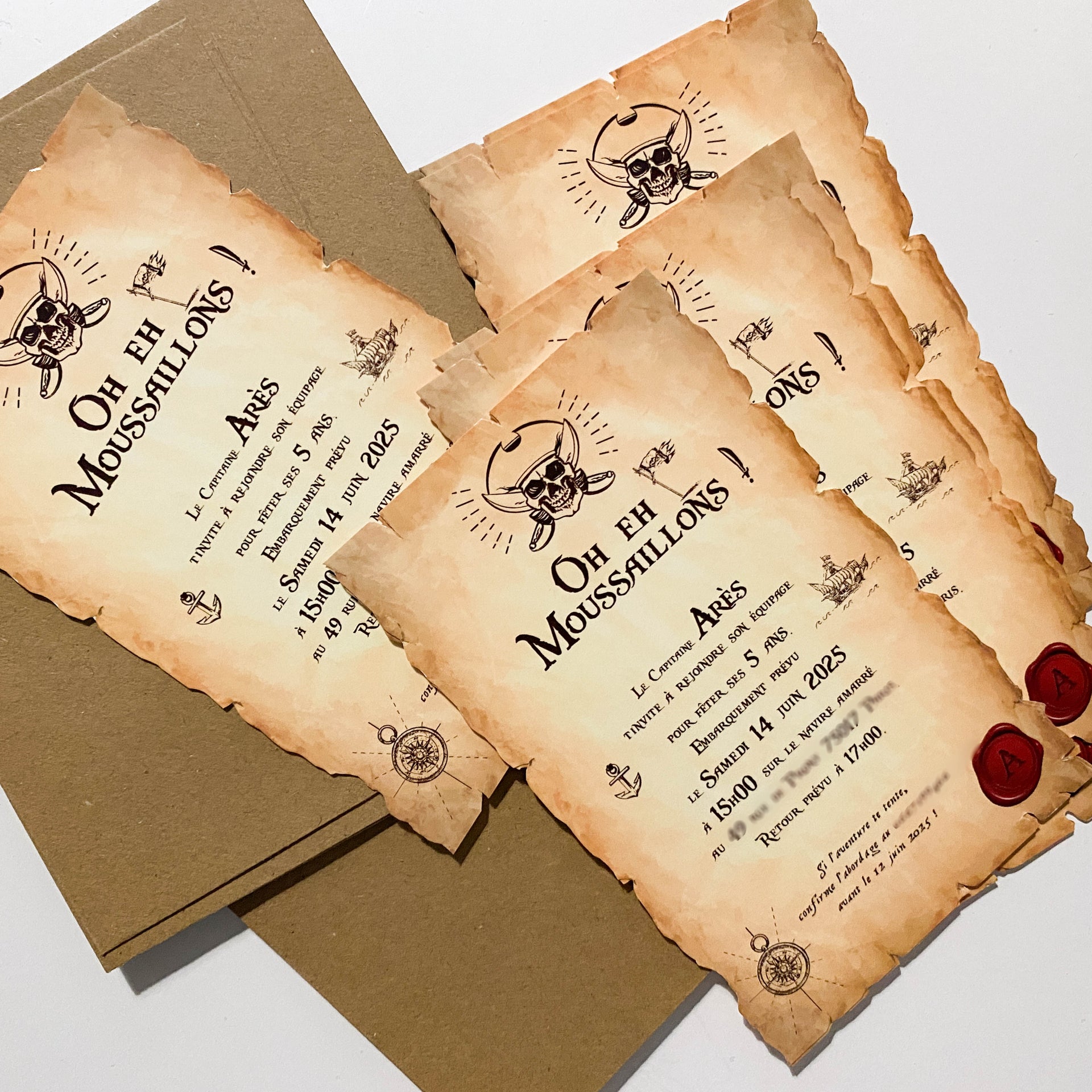 Photo d’invitations imprimées pirates style parchemin vieilli : bords brûlés, en-tête « Oh Eh Moussaillons ! », crâne avec sabres croisés, illustrations boussole/ancres/bateau, texte personnalisé (ex. Arès fête ses 5 ans, samedi 14 juin 2025 – 15h00–17h00), cachets de cire rouges, cartes posées avec enveloppes kraft.