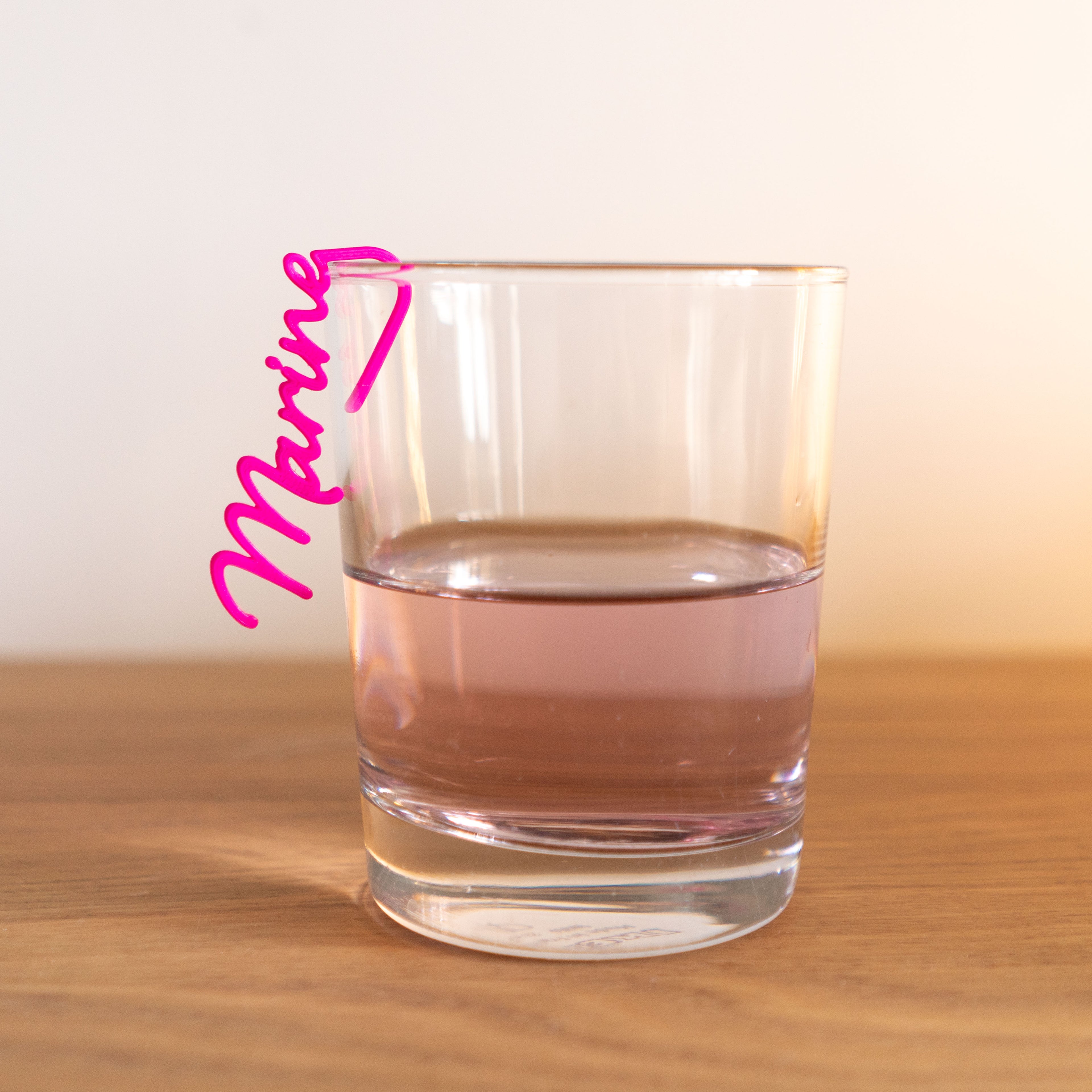Marque-verre personnalisé rose fuchsia au prénom "Marine" clipsé sur le rebord d'un verre, modèle Le Subtil en écriture cursive.