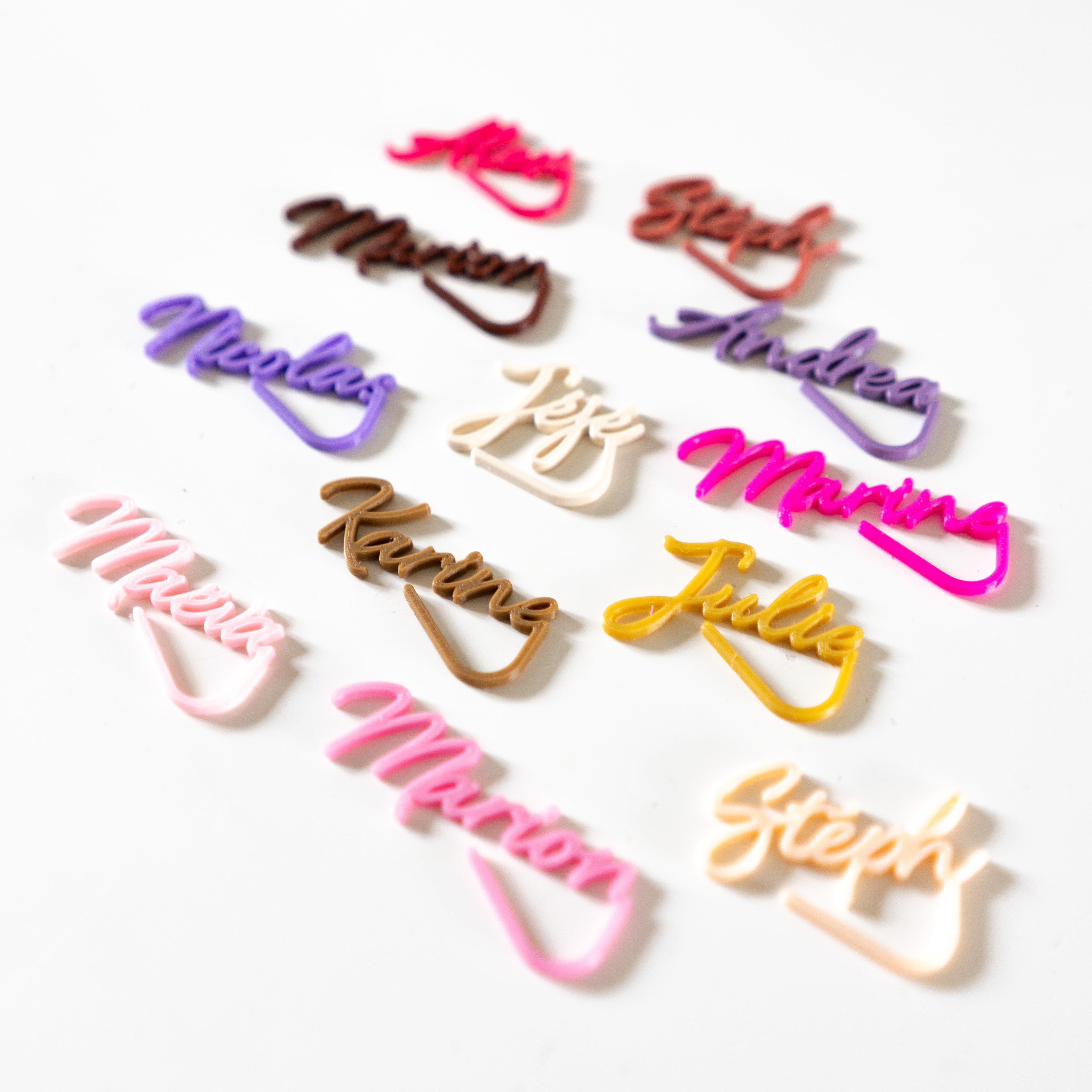 Marque-verres personnalisés Le Subtil en écriture cursive colorée (rose, jaune, violet) imprimés en 3D pour décoration de table de mariage.