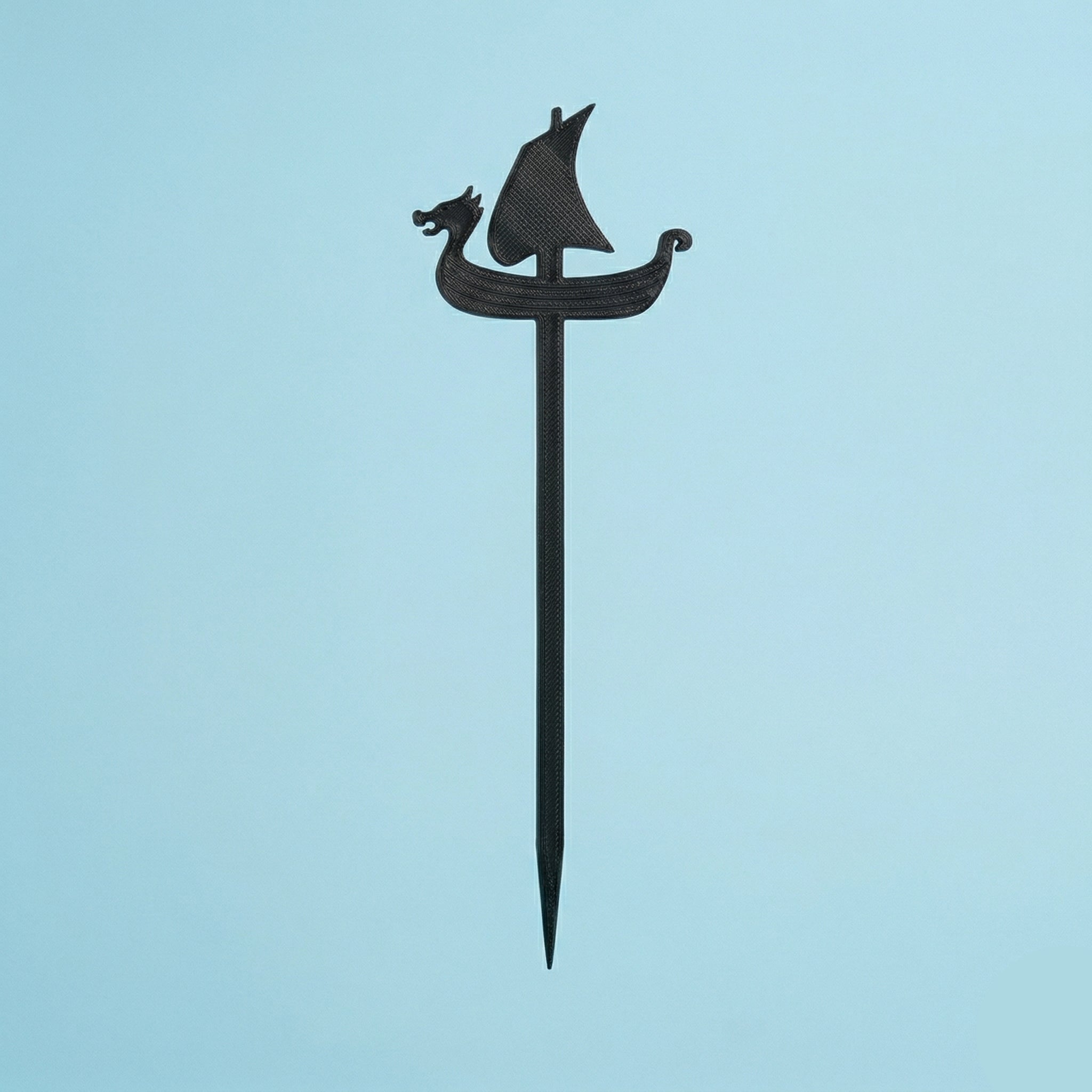 Une pique à mini-brochette noire en forme de drakkar viking avec une tête de dragon et une voile. Cet accessoire, réalisé en impression 3D, est présenté verticalement sur un fond bleu uni.