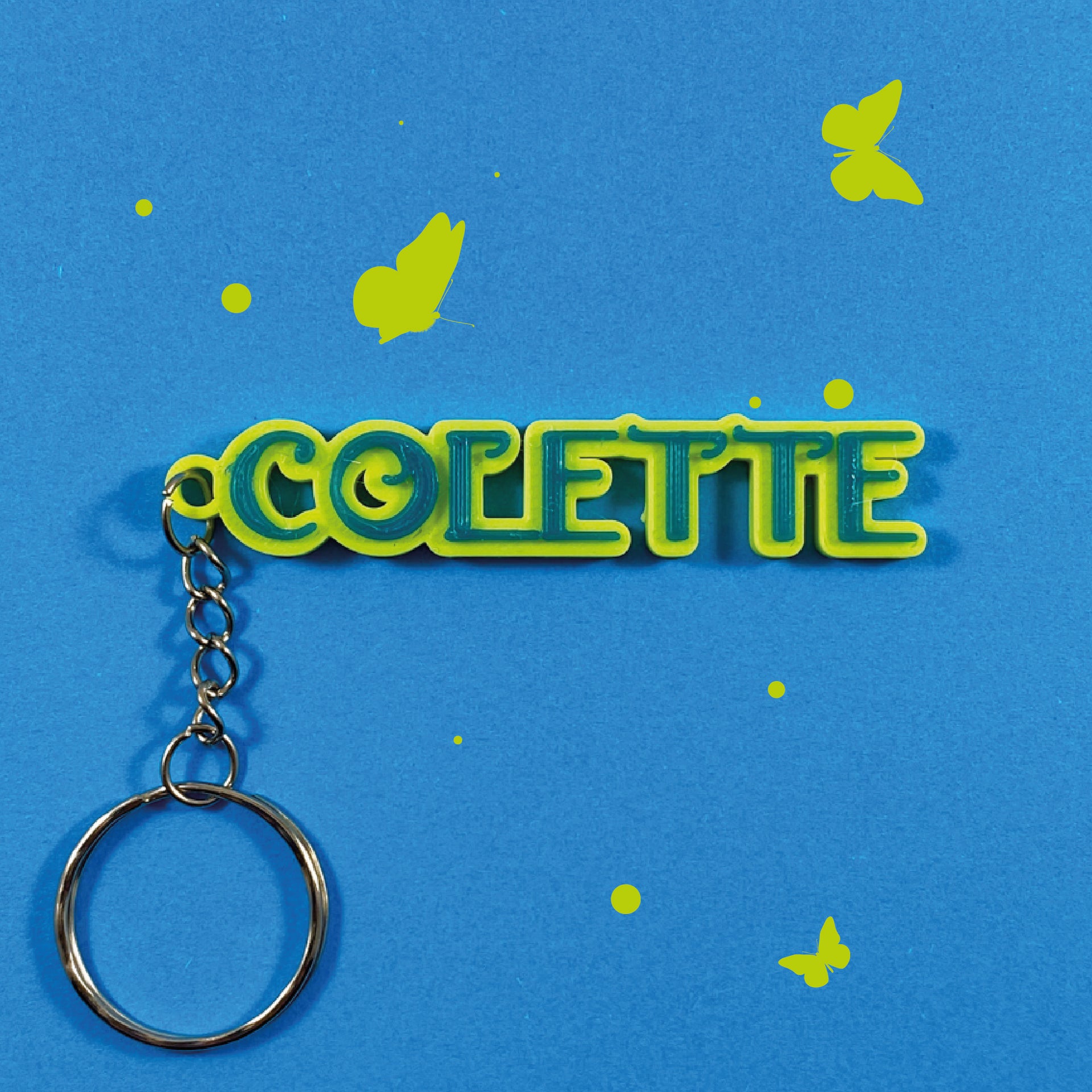 Porte-clés personnalisé au prénom Colette style Encanto en relief jaune et vert sur fond bleu avec illustrations de papillons.
