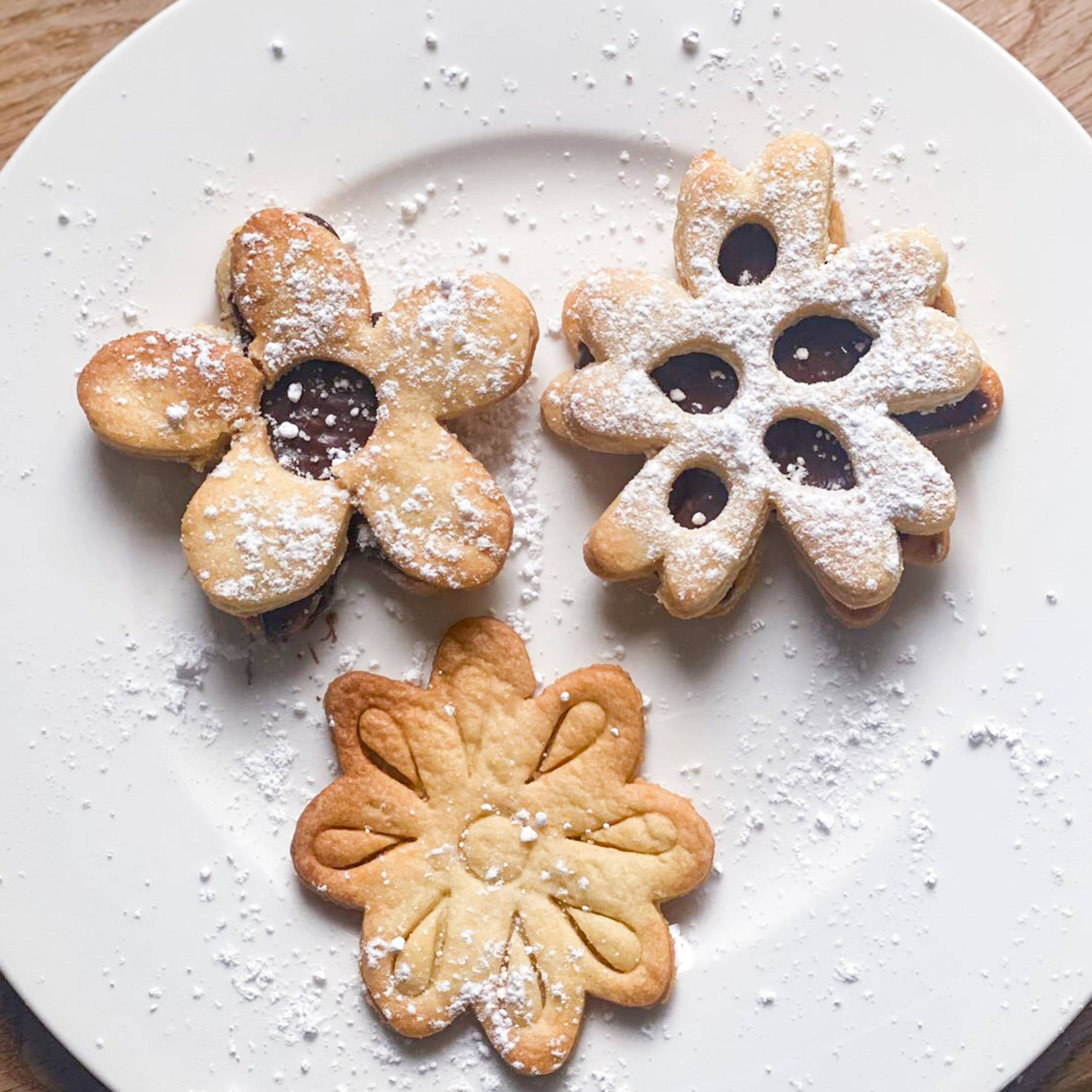 Biscuits fleurs fourrés au chocolat et saupoudrés de sucre glace, présentés sur une assiette pour un goûter créatif.
