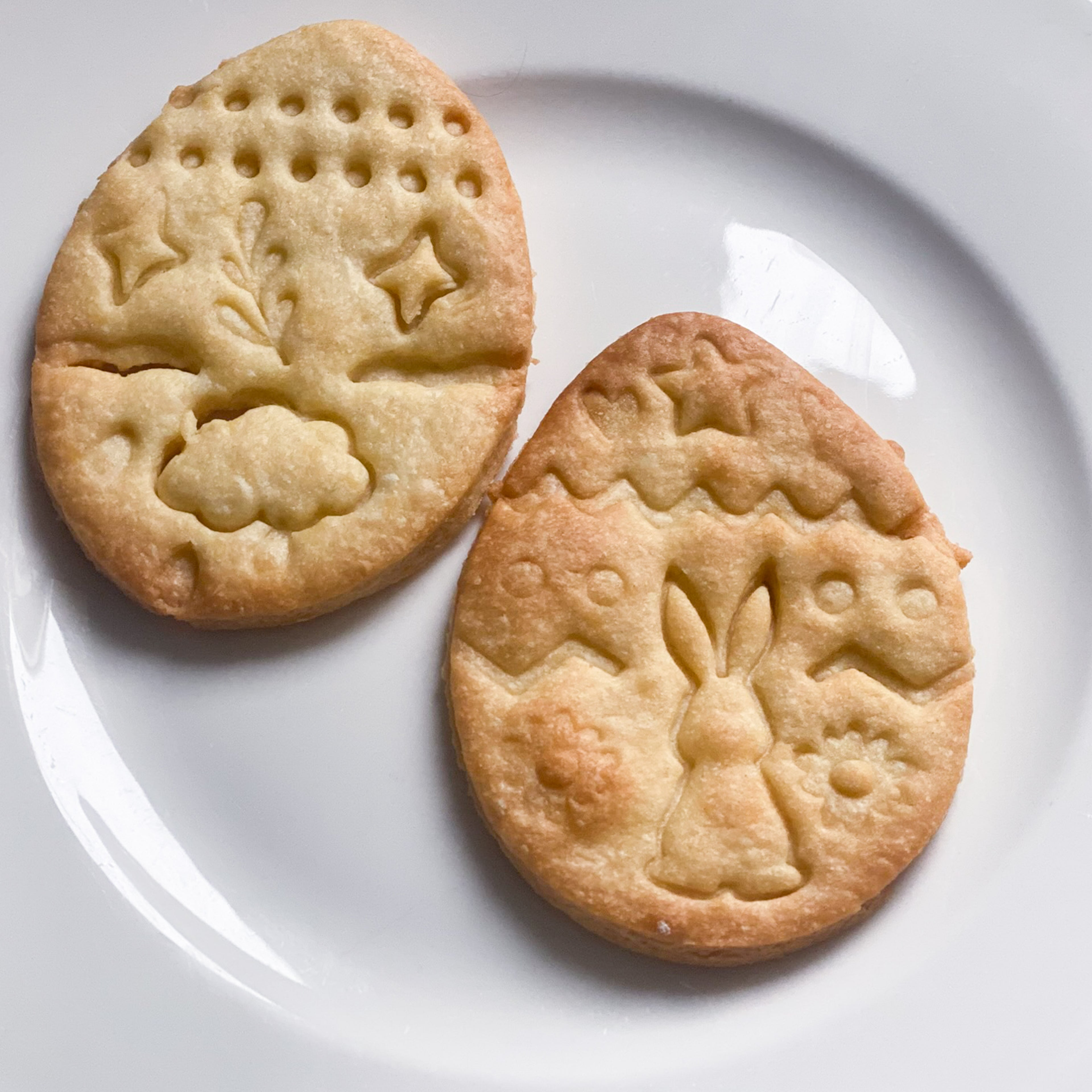 Biscuits de Pâques sablés en forme d'œufs avec décors gravés de lapin et fleurs prêts pour le goûter ou à offrir.