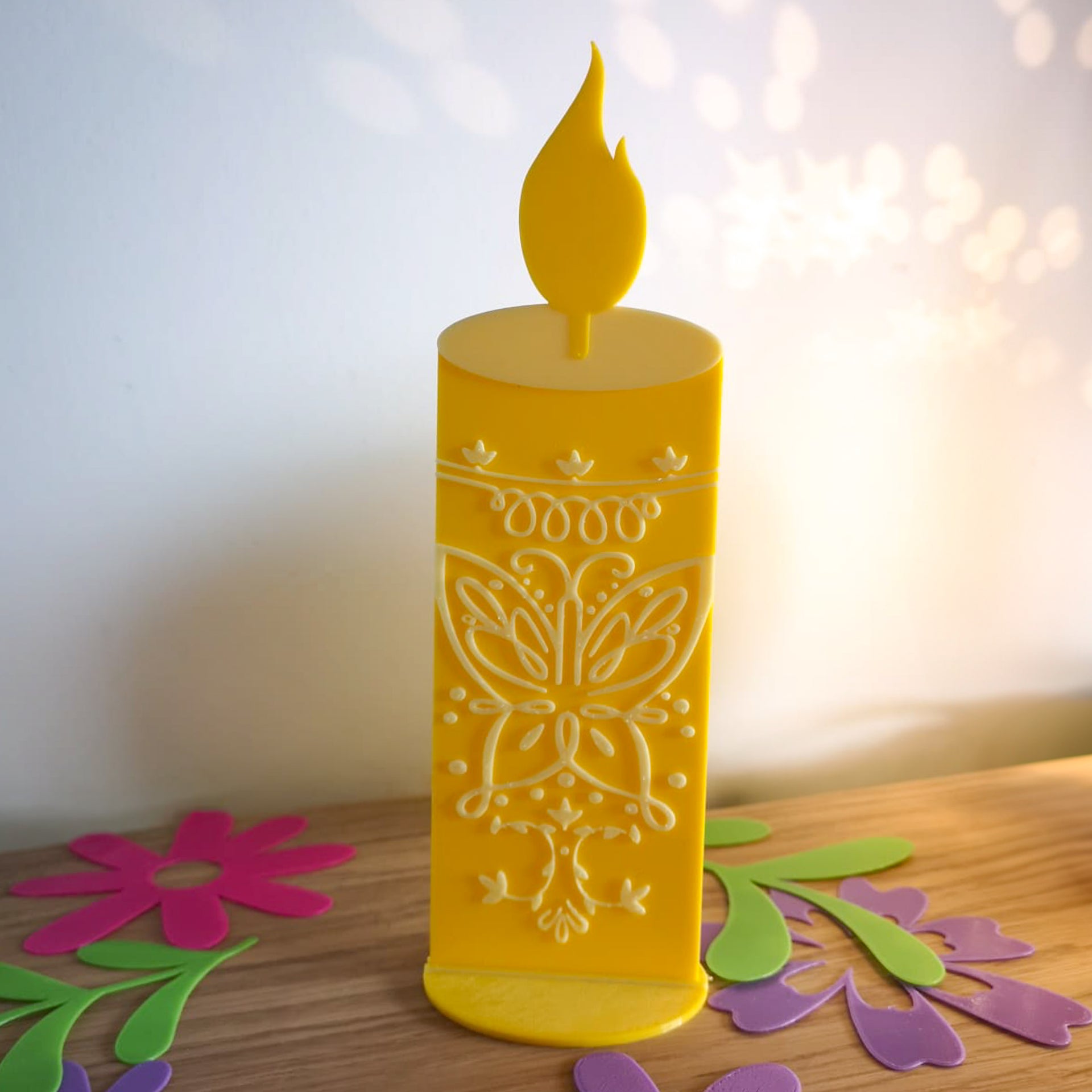 Décoration 3D en forme de bougie magique jaune inspirée du film Encanto, avec des motifs de papillon en relief blanc, posée sur un socle jaune sur un meuble en bois.