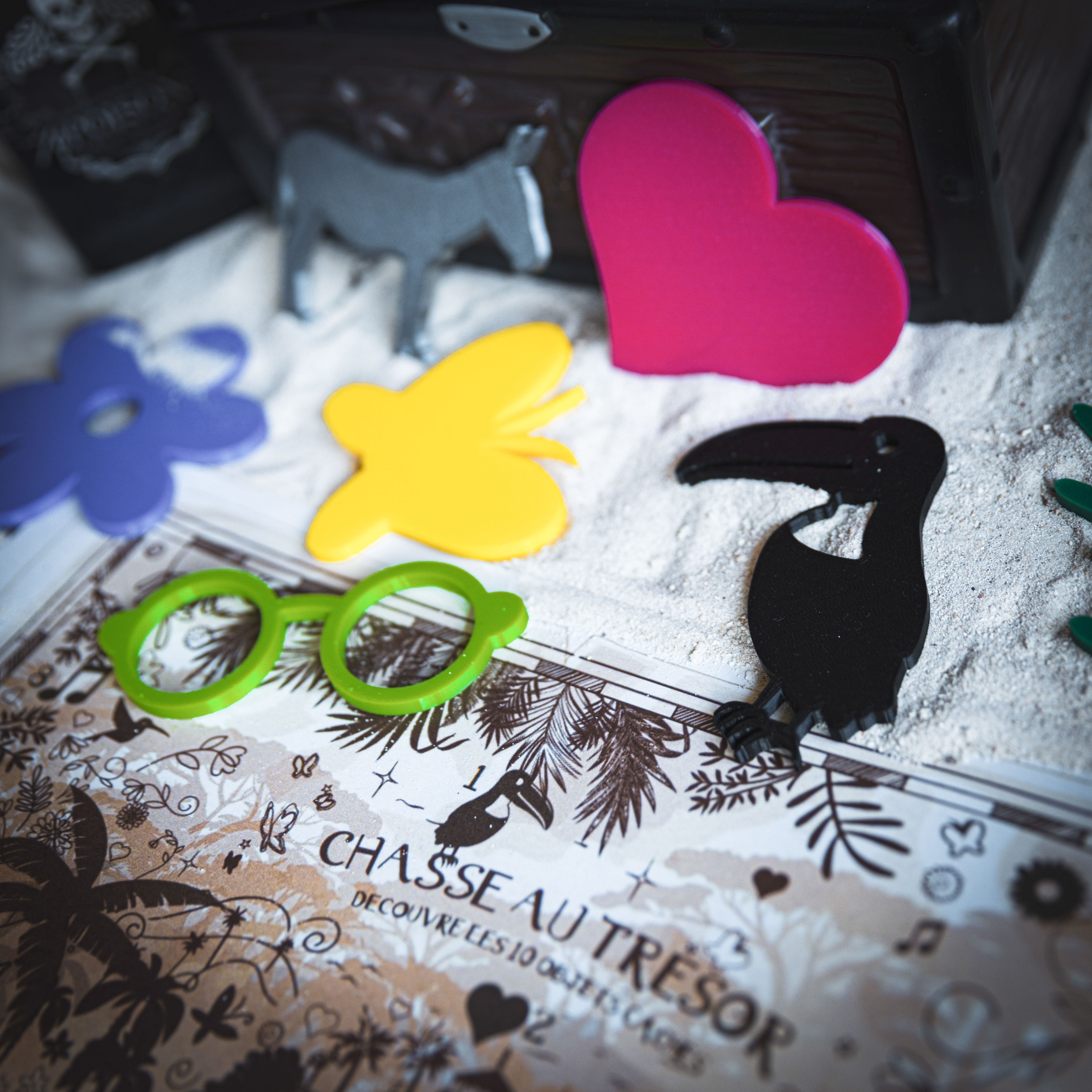 Chasse au trésor sur le thème Encanto avec carte à imprimer et objets 3D colorés à retrouver : lunettes vertes, papillon jaune, cœur rose, oiseau noir, âne gris et fleurs tropicales. Une activité ludique et immersive pour les enfants, parfaite pour un anniversaire enchanté.