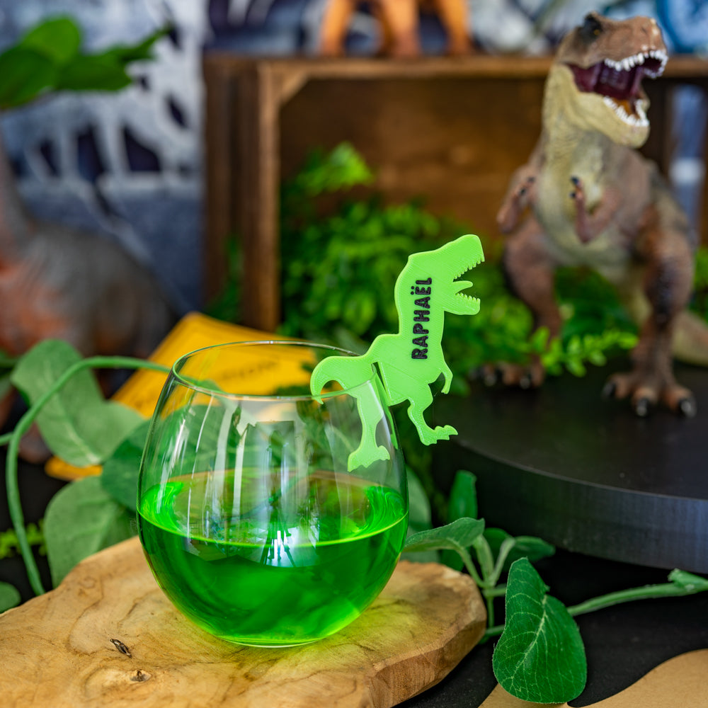 Marque-verre dinosaure T-Rex personnalisé en impression 3D, posé sur un verre pour une décoration d'anniversaire thème dinosaure.