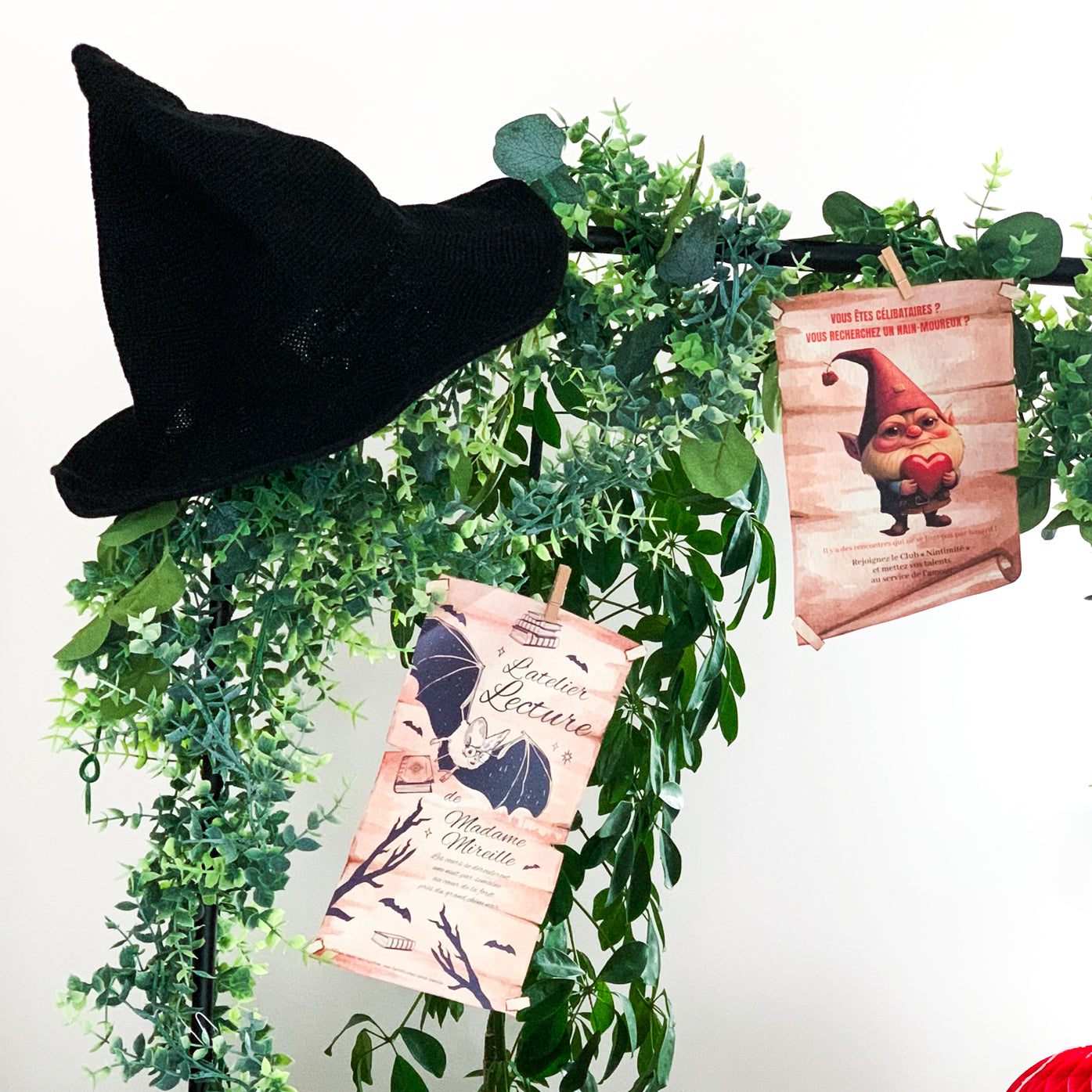 Décoration féerique avec feuillage, chapeau de sorcier noir et affiches humoristiques style parchemin, dont une annonce de rencontre pour nains et un atelier lecture avec chauve-souris – ambiance forêt enchantée