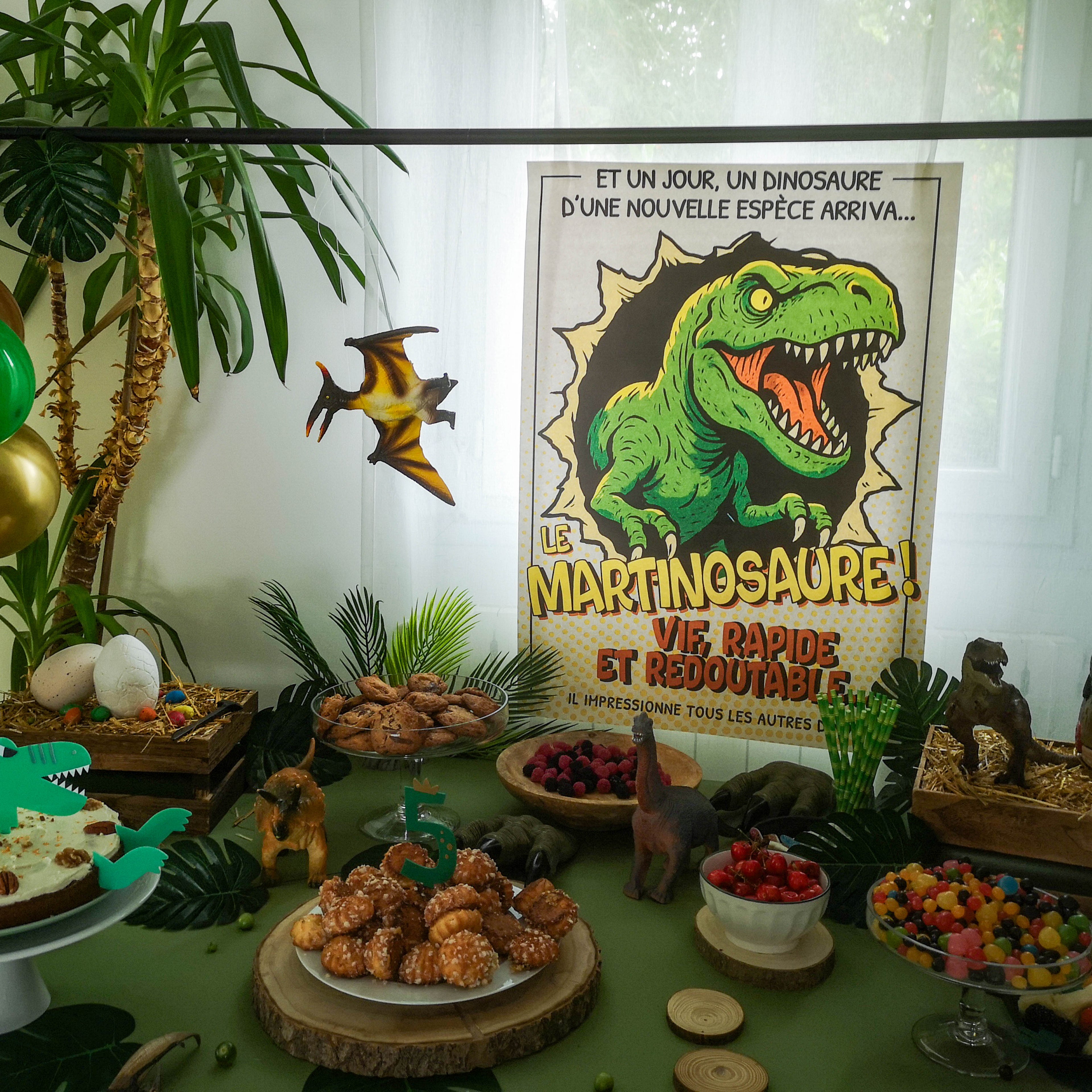 Décoration de buffet pour un anniversaire enfant sur le thème des dinosaures avec l'affiche personnalisée Martinosaure, des figurines et un goûter gourmand.