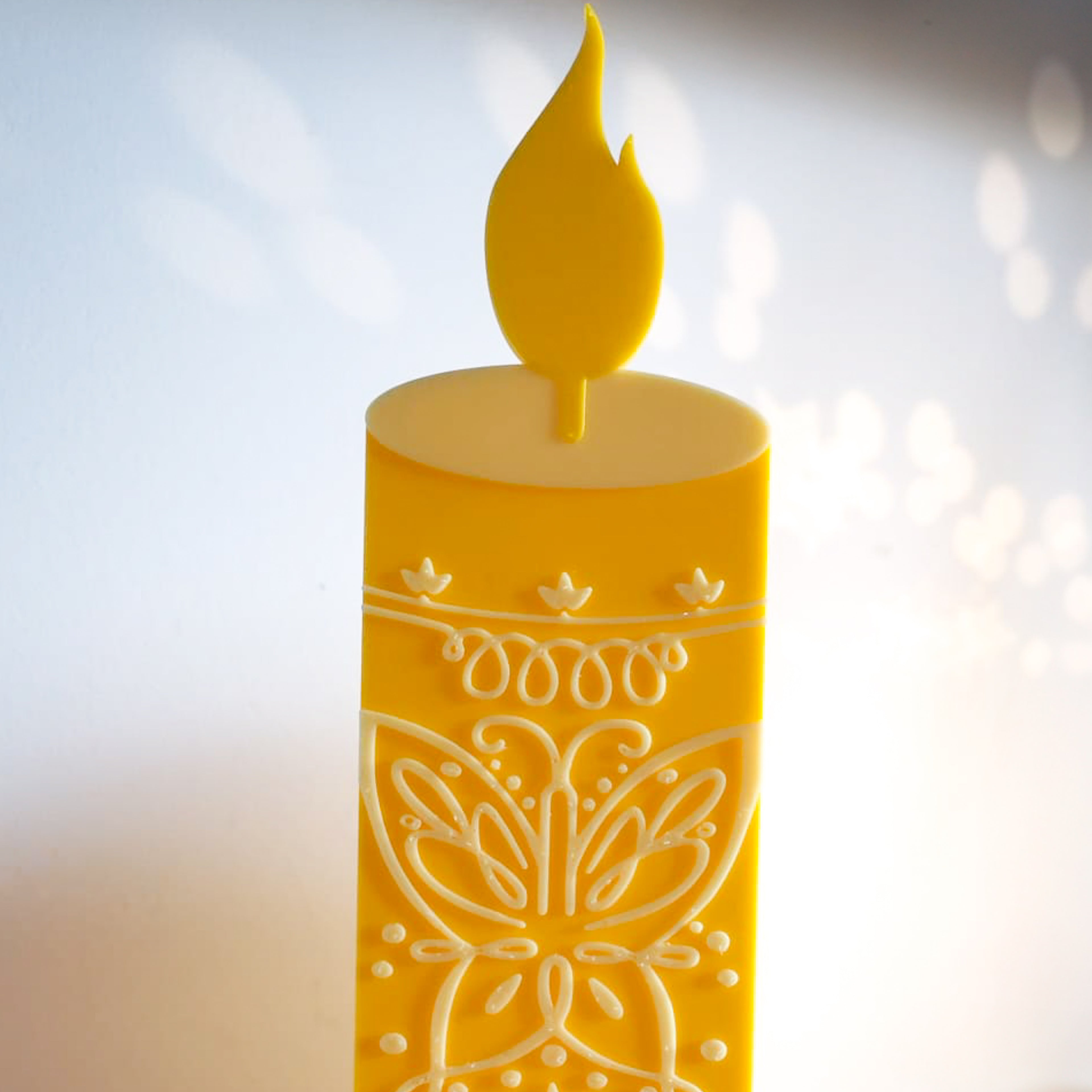 Gros plan sur les détails d'une bougie décorative jaune, mettant en avant les motifs de papillon et de volutes finement sculptés en relief blanc.