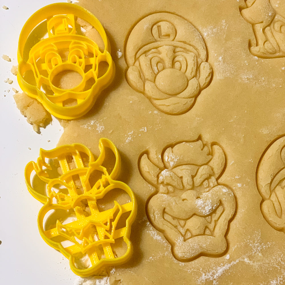 Empreintes de biscuits forme Mario Luigi Peach Toad et Bowser réalisées avec des emporte-pieces jaunes sur une pate sablée lors d’un atelier cuisine theme Heros du Royaume