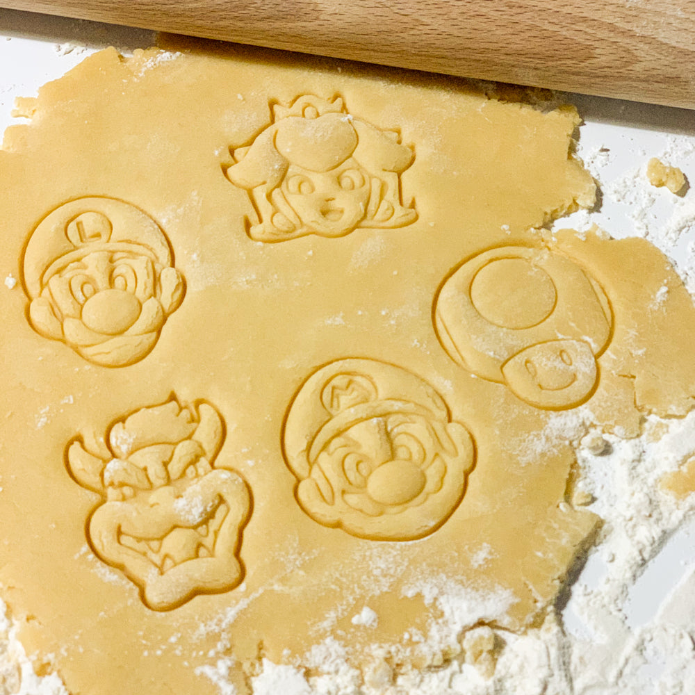 Empreintes de biscuits representant les personnages Mario, Luigi, Peach, Toad et Bowser dans une pate a sucre ou pate sablée, realisees avec des emporte-pieces du lot Heros du Royaume.
