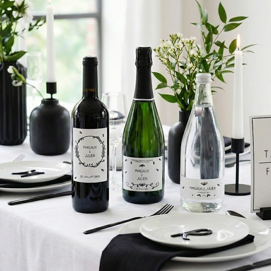 Trois bouteilles de mariage decorées avec des etiquettes noir et blanc personnalisables aux prenoms Margaux et Julien, sur une table chic avec vaisselle blanche et deco minimaliste.