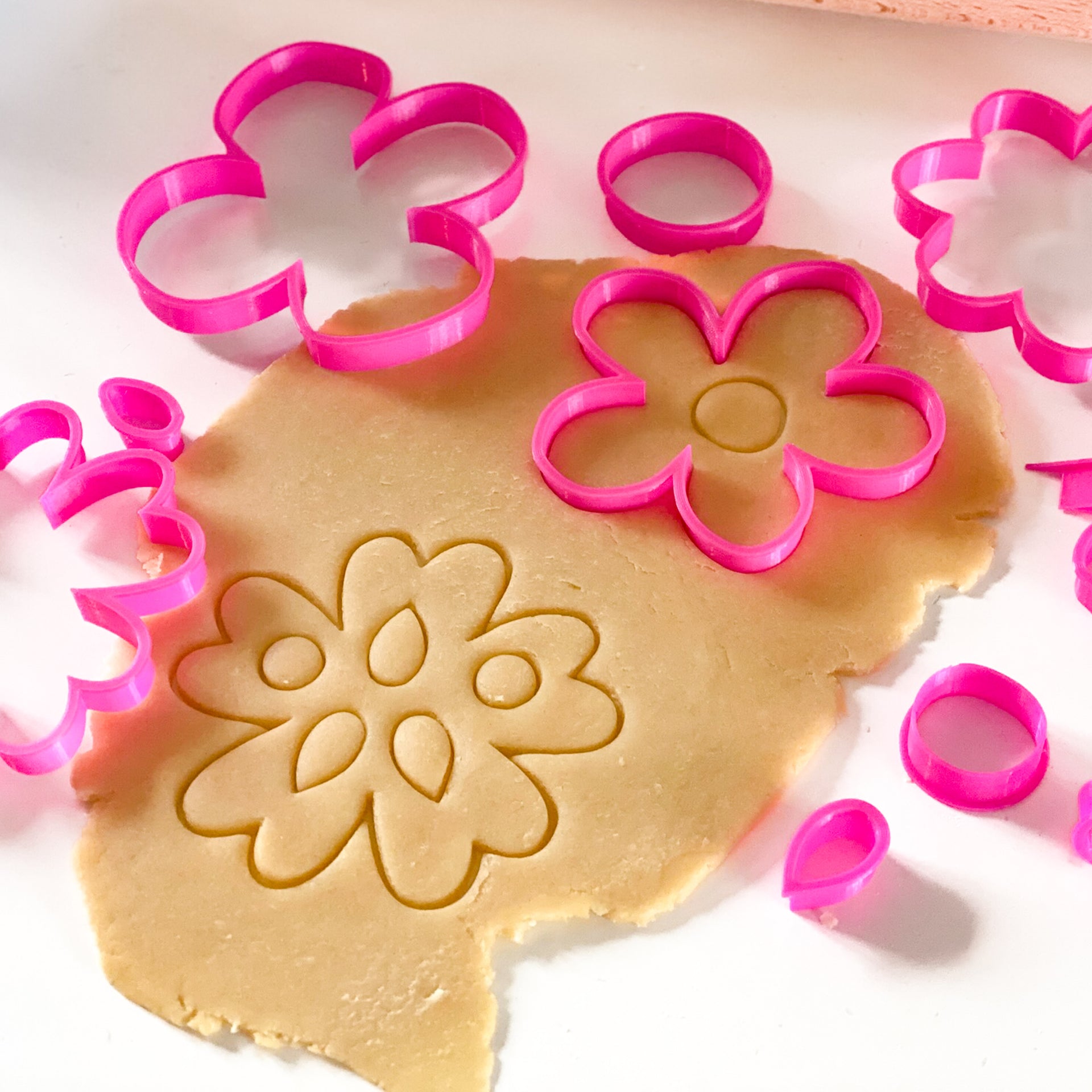 Kit d'emporte-pièces fleurs roses en relief sur une pâte à biscuits, idéal pour la pâtisserie créative et les ateliers enfants.