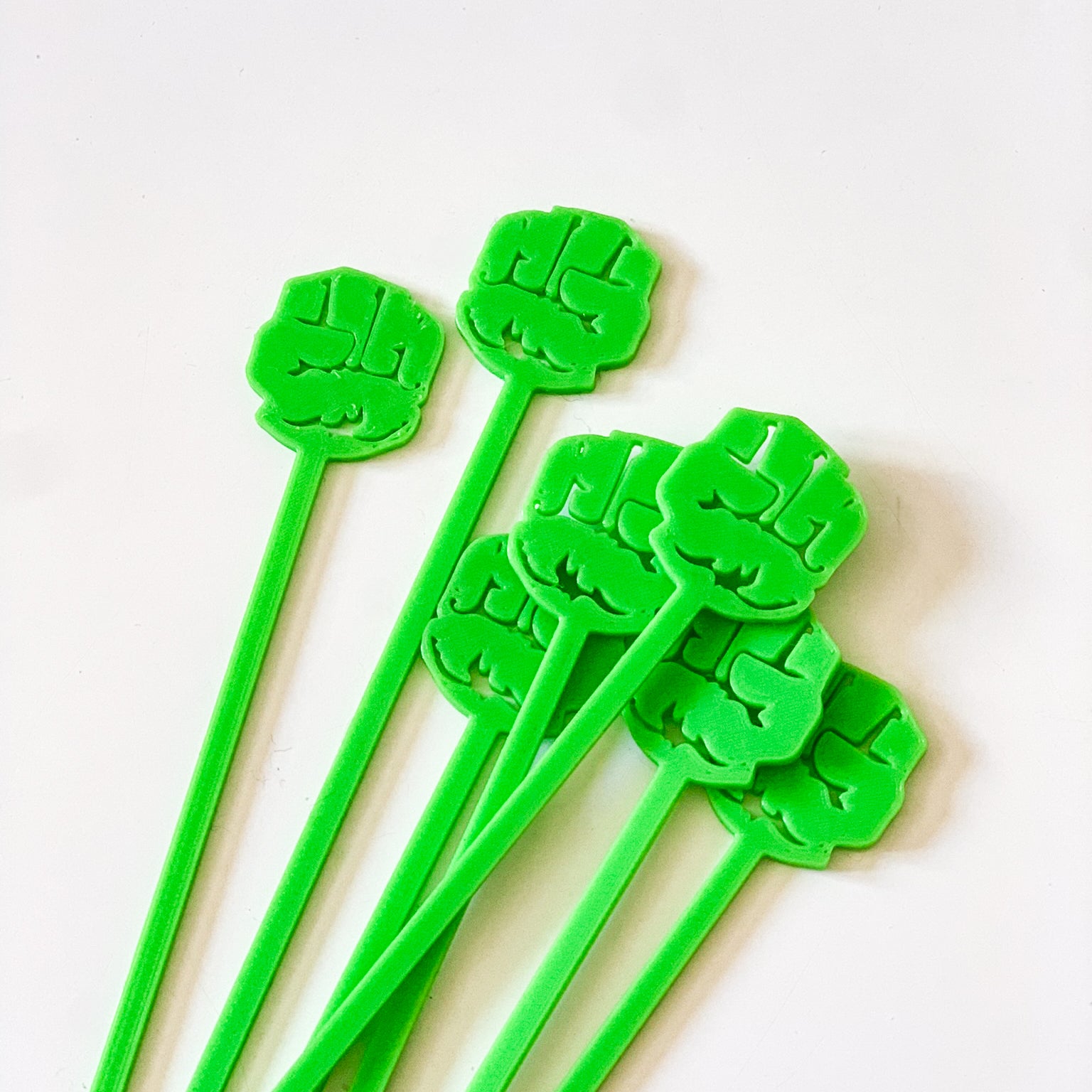 Lot de piques aperitif vert pomme en forme de poing de Hulk en impression 3D disposees en eventail sur fond blanc.