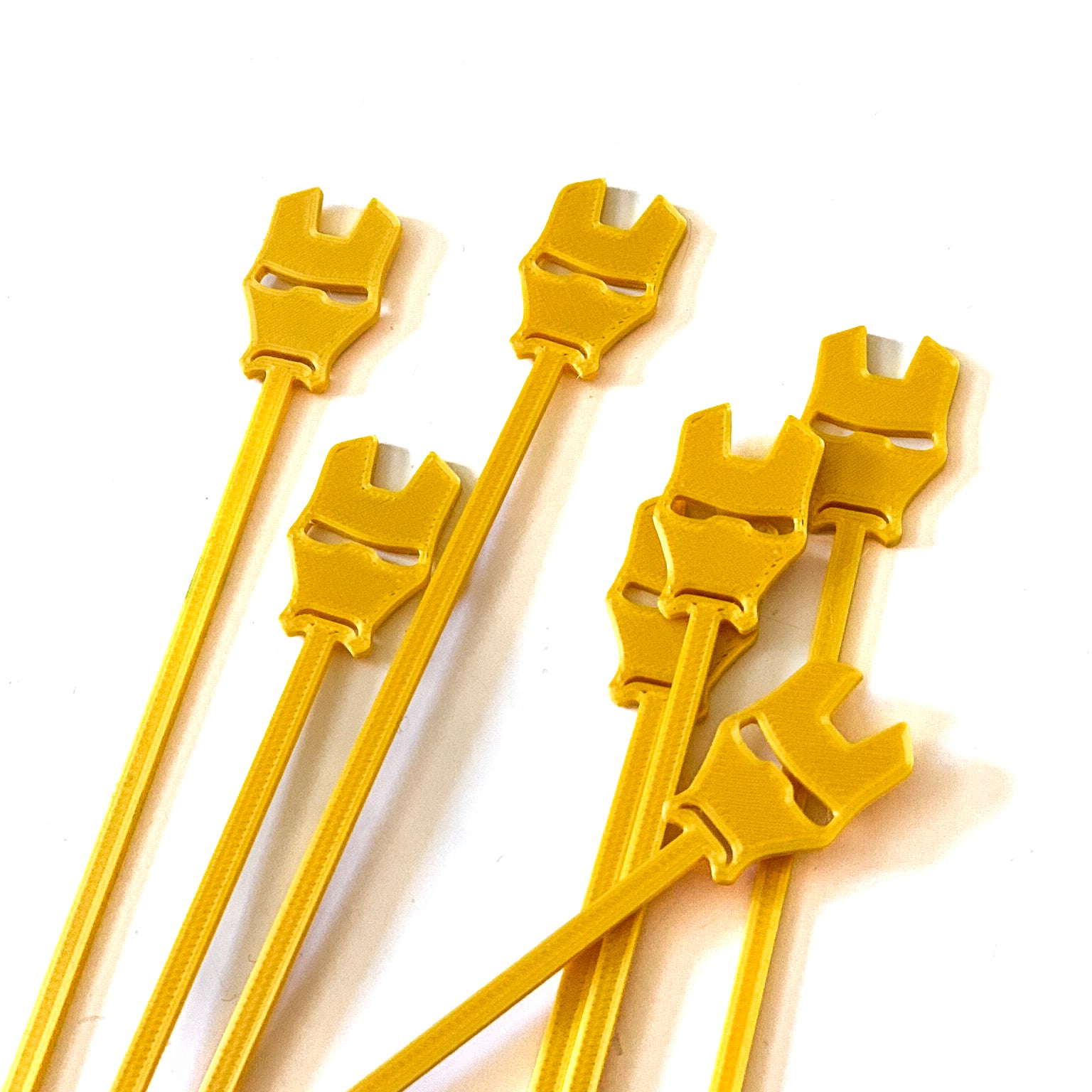 Lot de 8 piques apéritif dorées en forme de masque d'Iron Man en impression 3D pour décoration de buffet anniversaire super-héros.