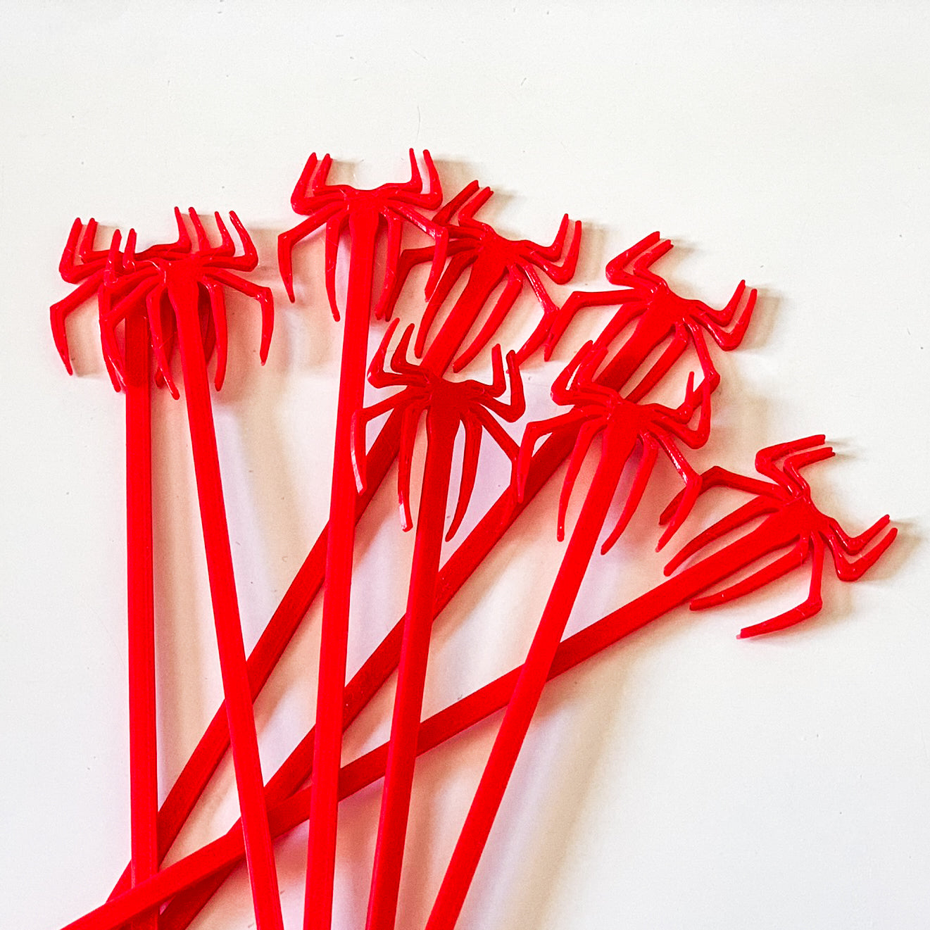 Lot de piques aperitif rouges en forme d'araignee Spider-Man en impression 3D disposees en eventail sur fond blanc.