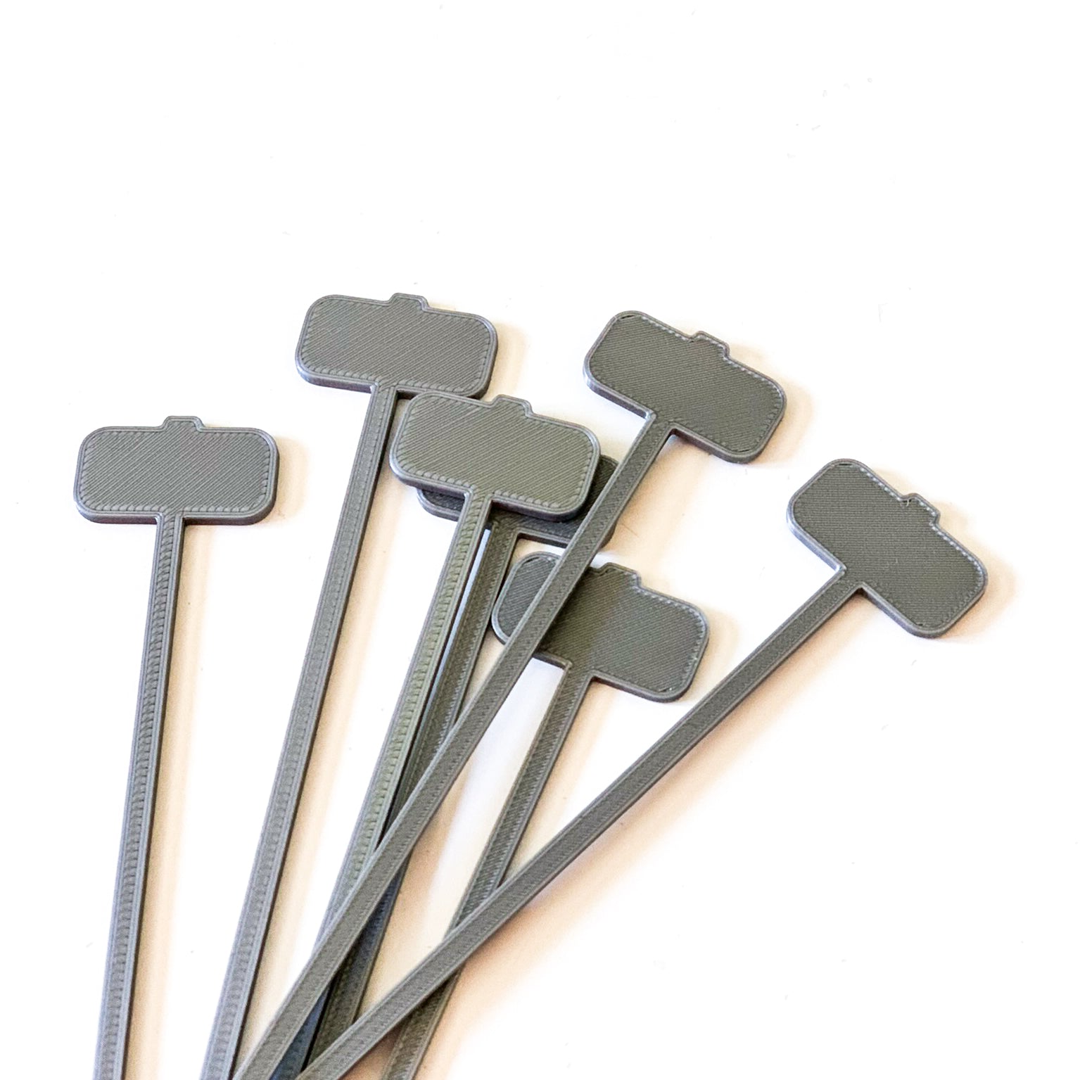 Lot de piques aperitif argentées en forme de marteau de Thor Mjölnir en impression 3D disposees en eventail sur fond blanc.