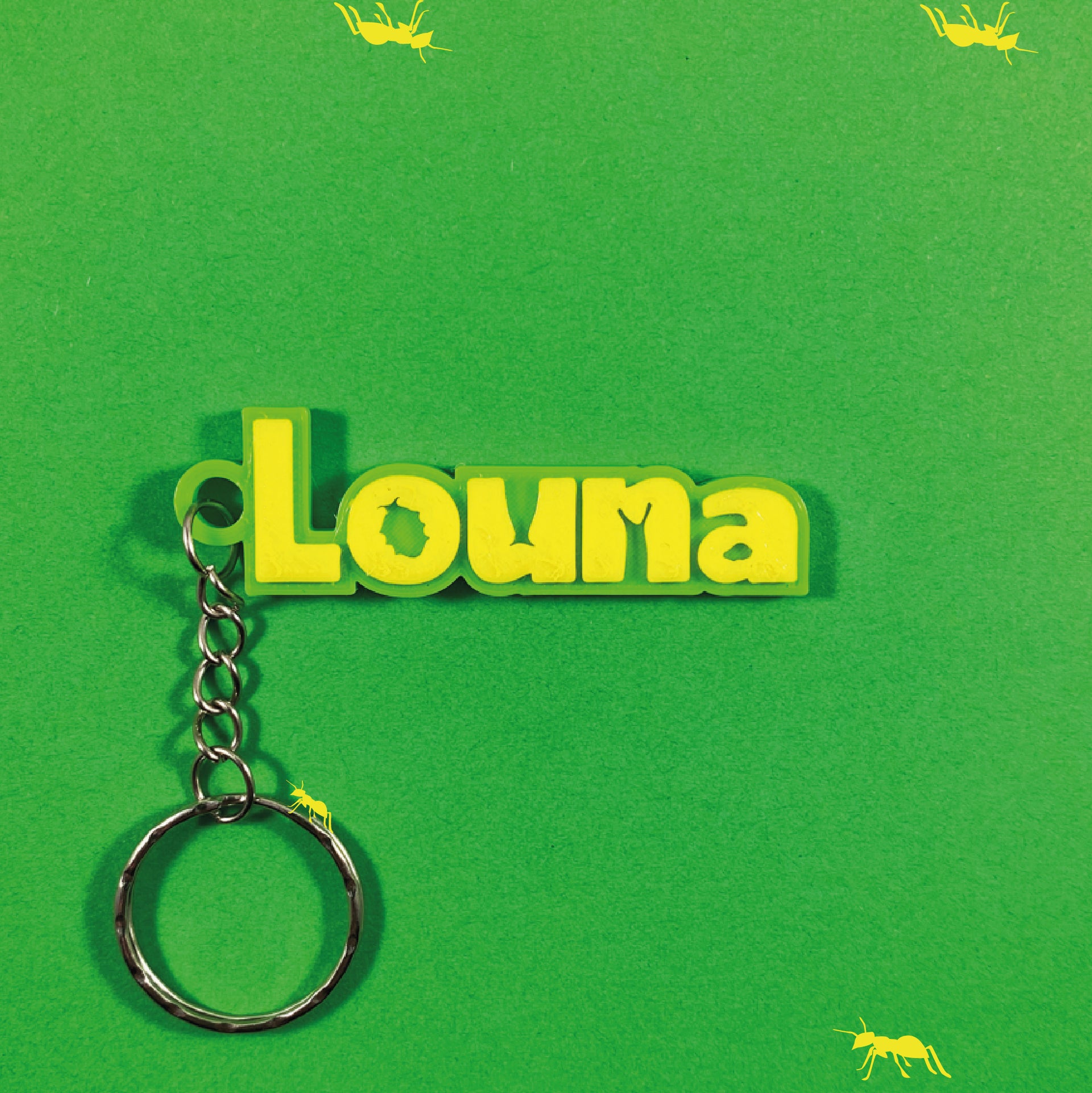 Porte-clés personnalisé "Louna" en relief jaune sur plaque vert citron, style 1001 pattes - insectes, sur fond vert décoré de silhouettes de fourmis jaunes. Un point bleu est visible.
