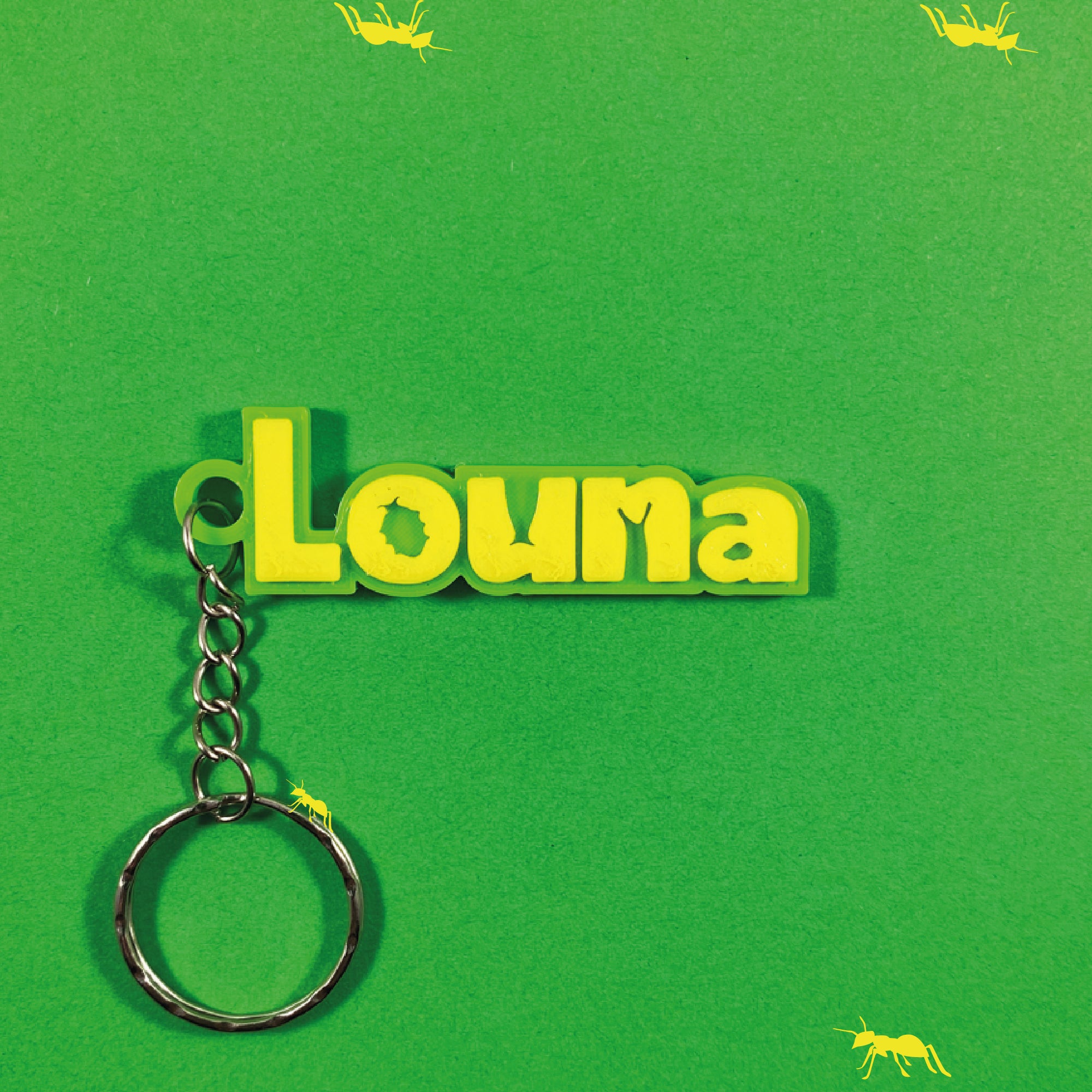 Porte-clés personnalisé "Louna" en relief jaune sur plaque vert citron, style 1001 pattes - insectes, sur fond vert décoré de silhouettes de fourmis jaunes. Un point bleu est visible.