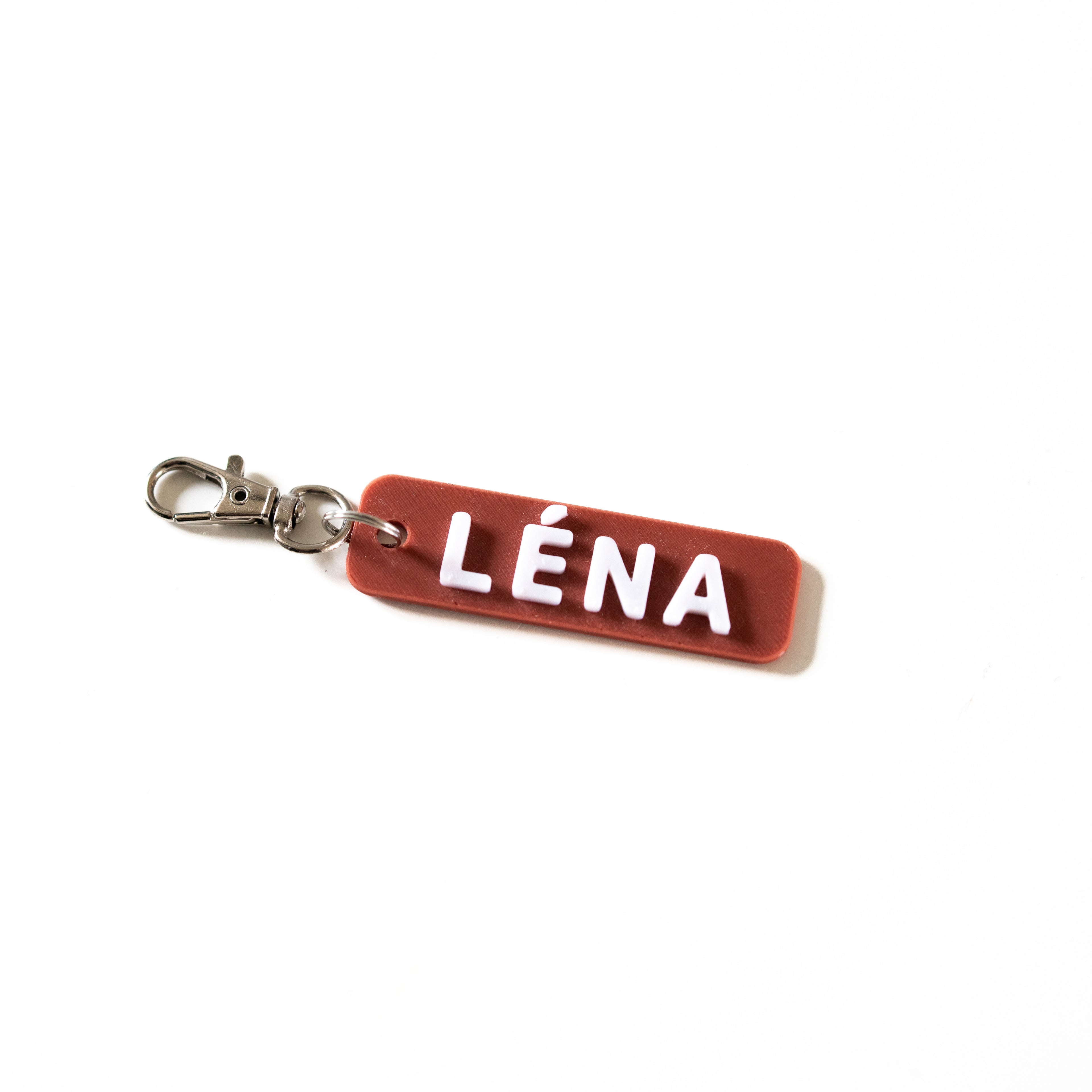 Porte-clé personnalisé en impression 3D avec le prénom LÉNA en relief blanc sur une base couleur terre cuite. Accessoire bicolore avec attache mousqueton argentée sur fond blanc.