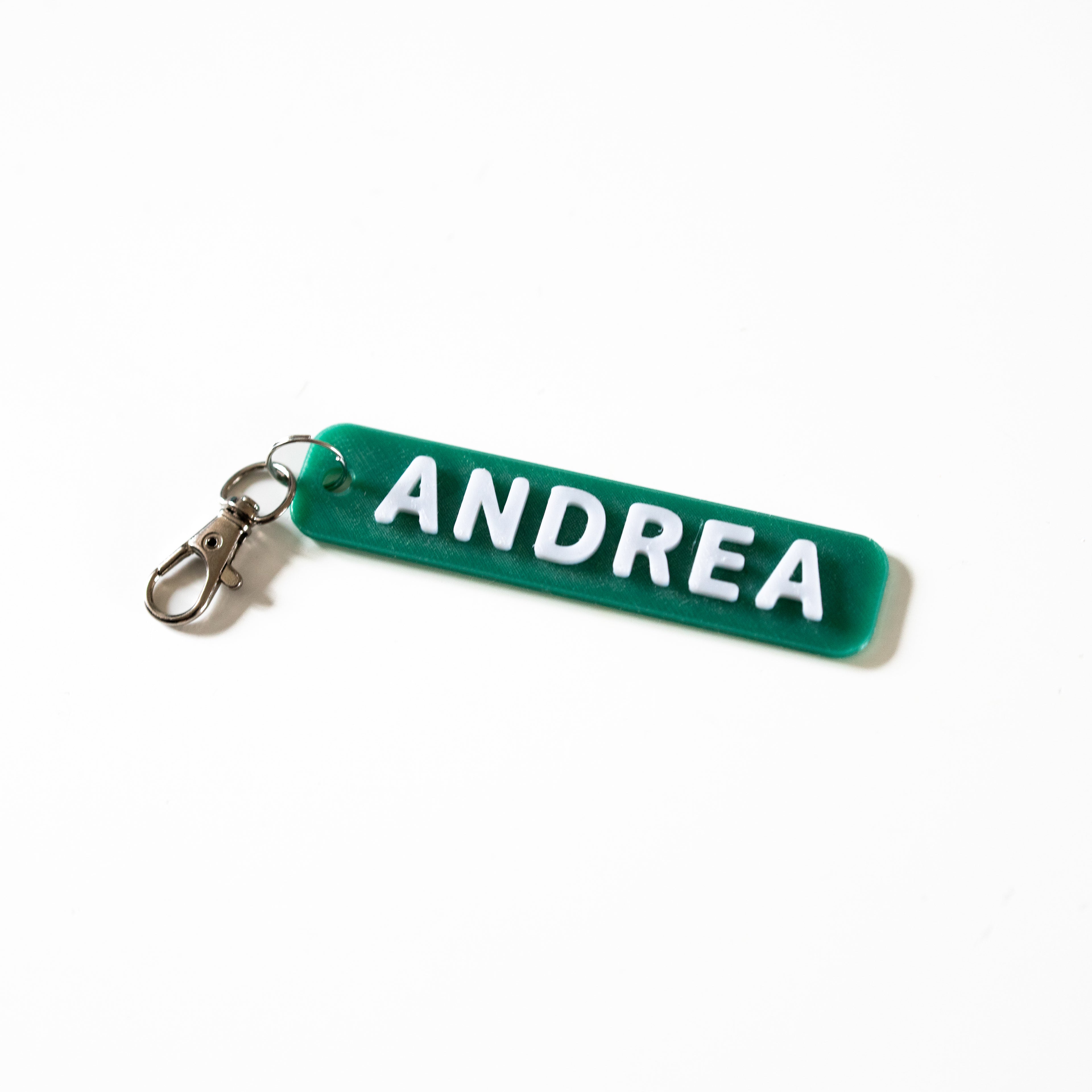 Porte-clé personnalisé en impression 3D avec le prénom ANDREA en relief blanc sur une base vert émeraude. Design bicolore avec attache mousqueton argentée, idéal pour personnaliser un sac ou un trousseau de clés.