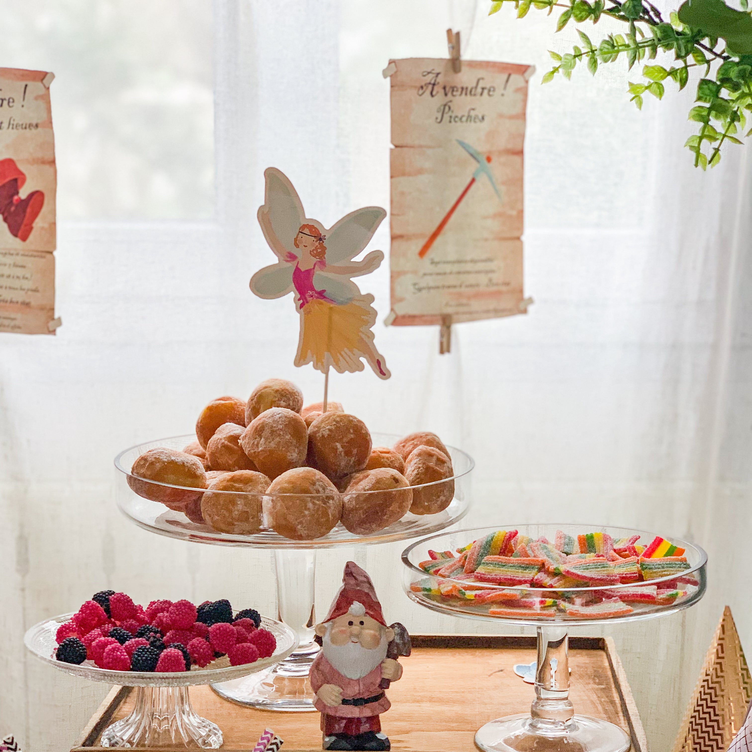Table de goûter féerique avec fée en décoration, bonbons, beignets, et affiches humoristiques inspirées de la forêt enchantée, ambiance magique pour fête d’enfant
