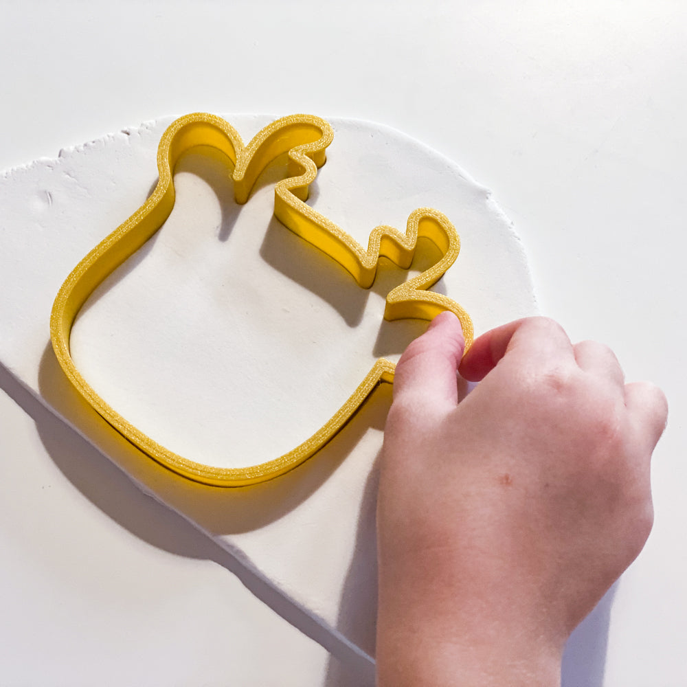 Enfant utilisant un emporte-piece renne jaune pour decouper une forme dans de la pate autodurcissante, activite creative de Noel.