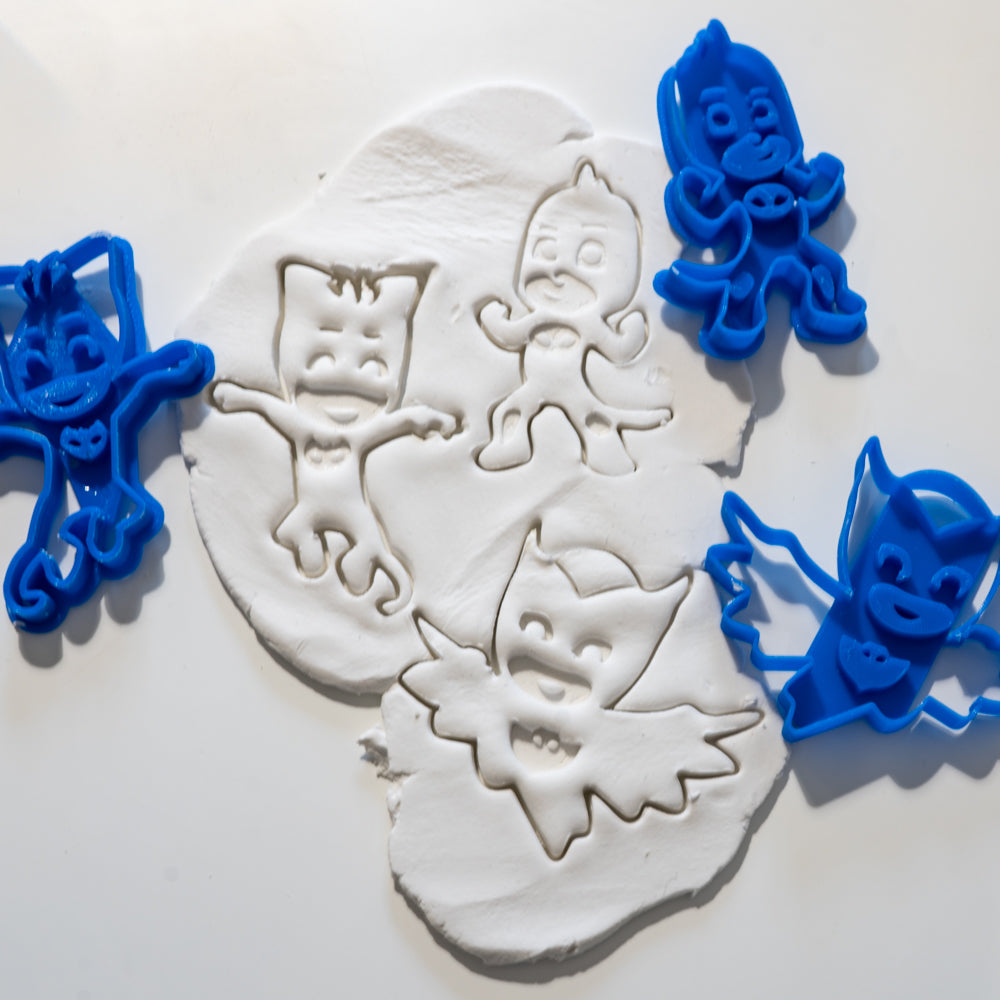 Empreintes de biscuits Pyjamasques dans la pâte avec les emporte-pièces bleus représentant Sacha, Amaya et Greg du lot “Héros de la Nuit”.