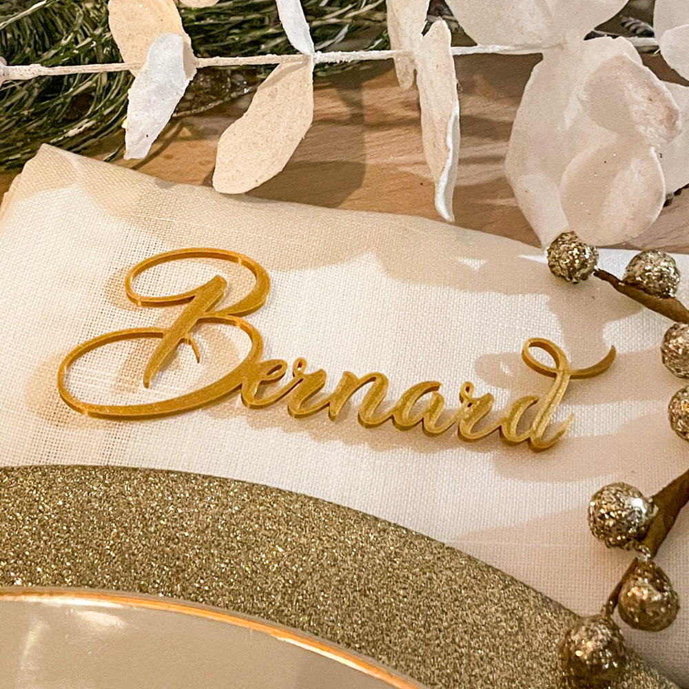 Marque-place en écriture calligraphique dorée posé sur une serviette blanche, idéal pour sublimer une décoration de table élégante.