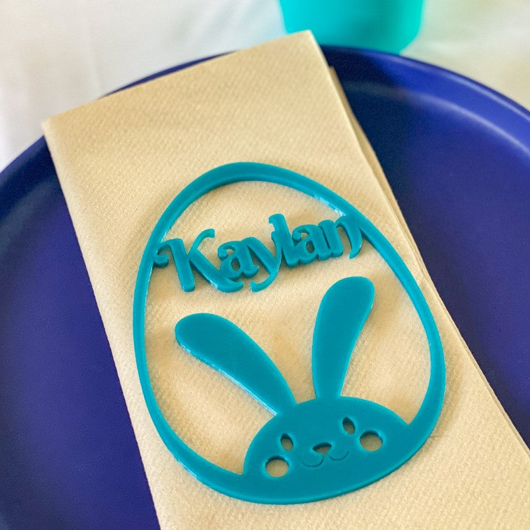 Marque-place de Pâques en forme d’œuf avec lapin et prénom « Kaylan » découpé dans la forme, posé sur une serviette pour une décoration de table festive.