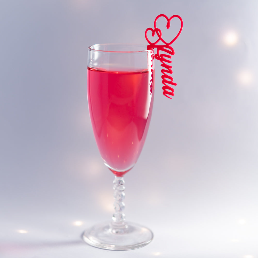 Verre de fête décoré d’un marque-verre Double Cœur rouge personnalisé avec le prénom Lynda, accroché élégamment au bord du verre rempli d’une boisson rose.