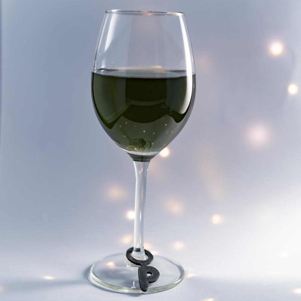 Verre à pied équipé d’un marque-verre noir en forme de grande initiale attachée autour du pied, permettant d’identifier facilement son verre.