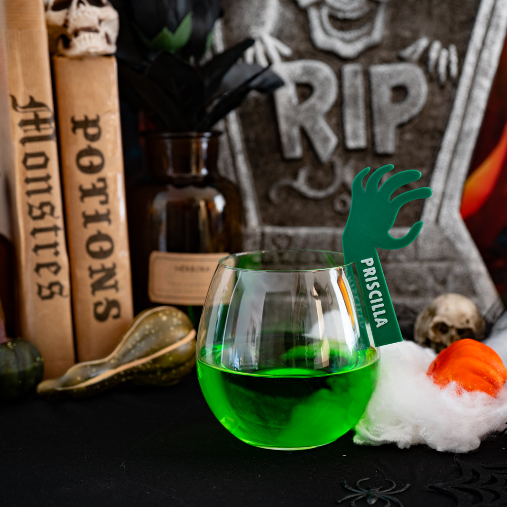 Marque-verre Halloween en forme de bras de mort vivant vert, accroché au bord d’un verre et personnalisé avec un prénom.