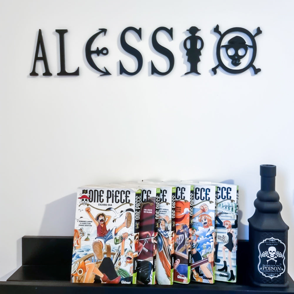 Prénom “ALESSIO” en décoration murale, réalisé en impression 3D (PLA) noire, inspiré de l’univers One Piece avec ancre, silhouette de pirate et motif tête de mort, présenté au-dessus d’étagères avec mangas.