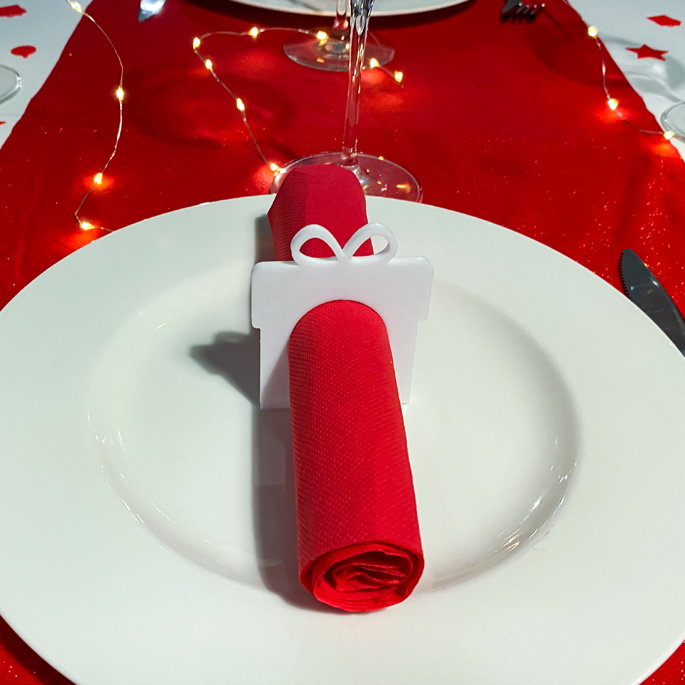 Rond de serviette en forme de cadeau utilisé pour une décoration de table de Noël, avec serviette rouge et ambiance lumineuse festive.