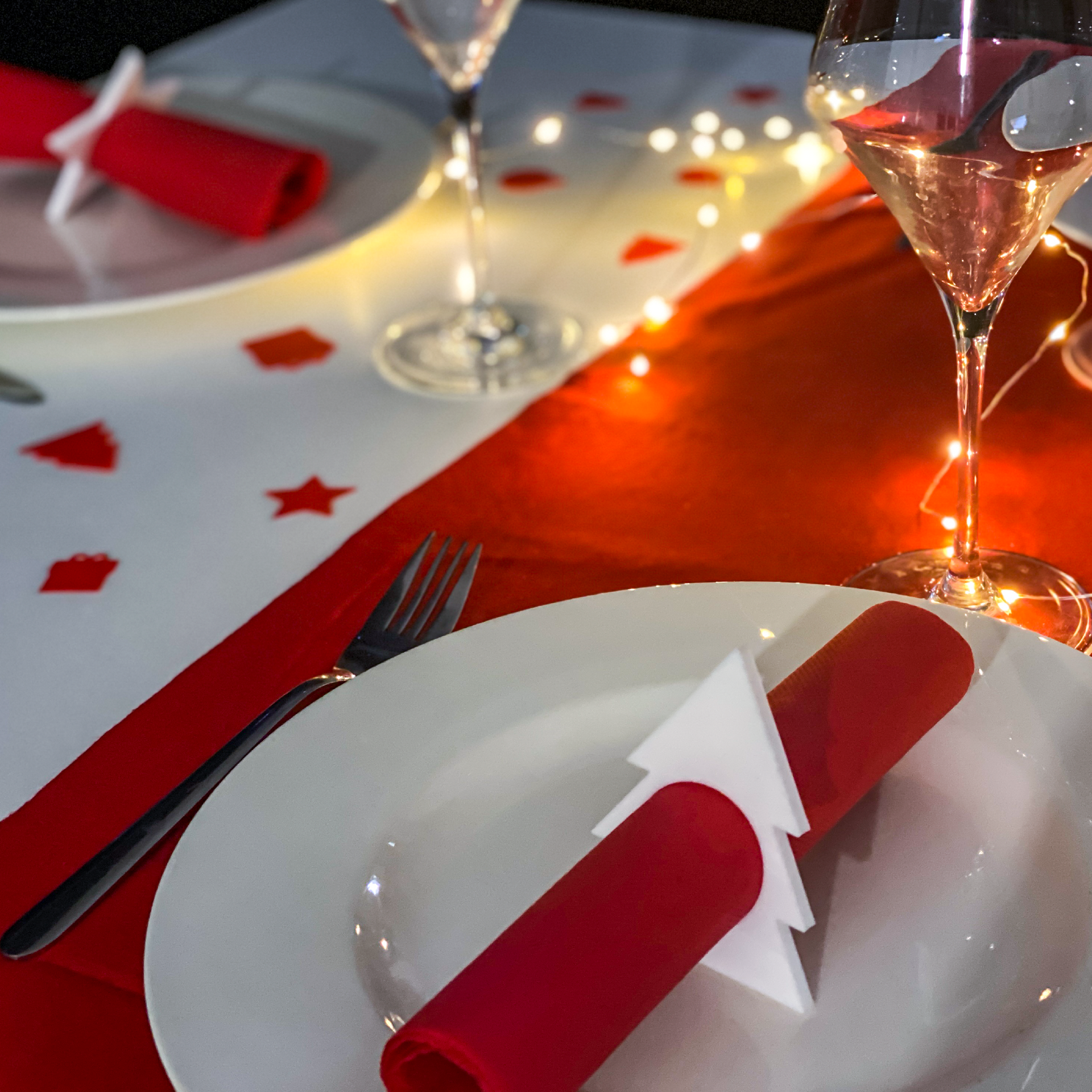 Rond de serviette en forme de sapin utilisé pour une décoration de table de Noël, avec serviette rouge et ambiance lumineuse festive. Au fond, forme Etoile.