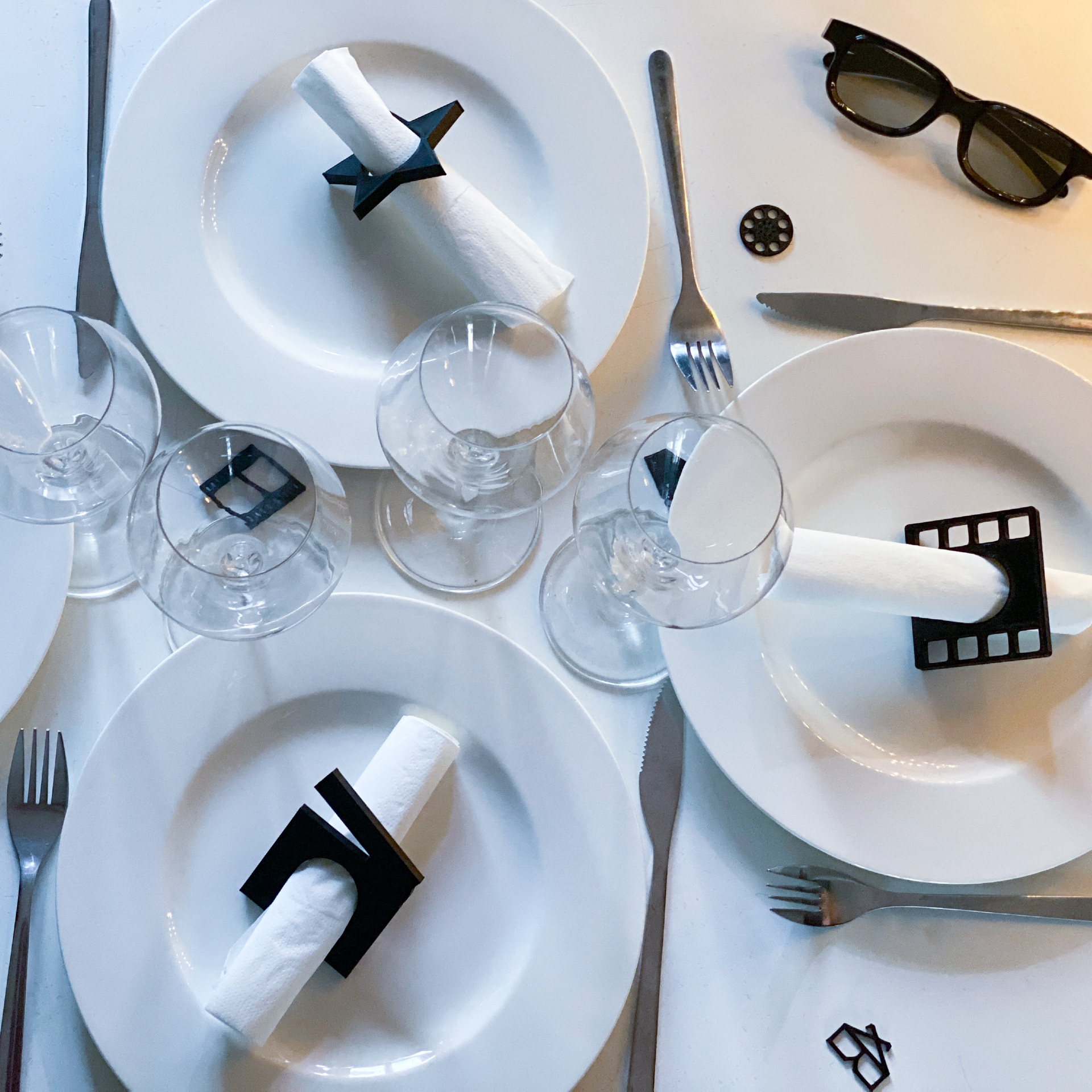 Ronds de serviette thème cinéma disposés sur une table blanche avec assiettes et verres, modèles étoile, clap, pellicule et bobine pour une décoration de fête stylée