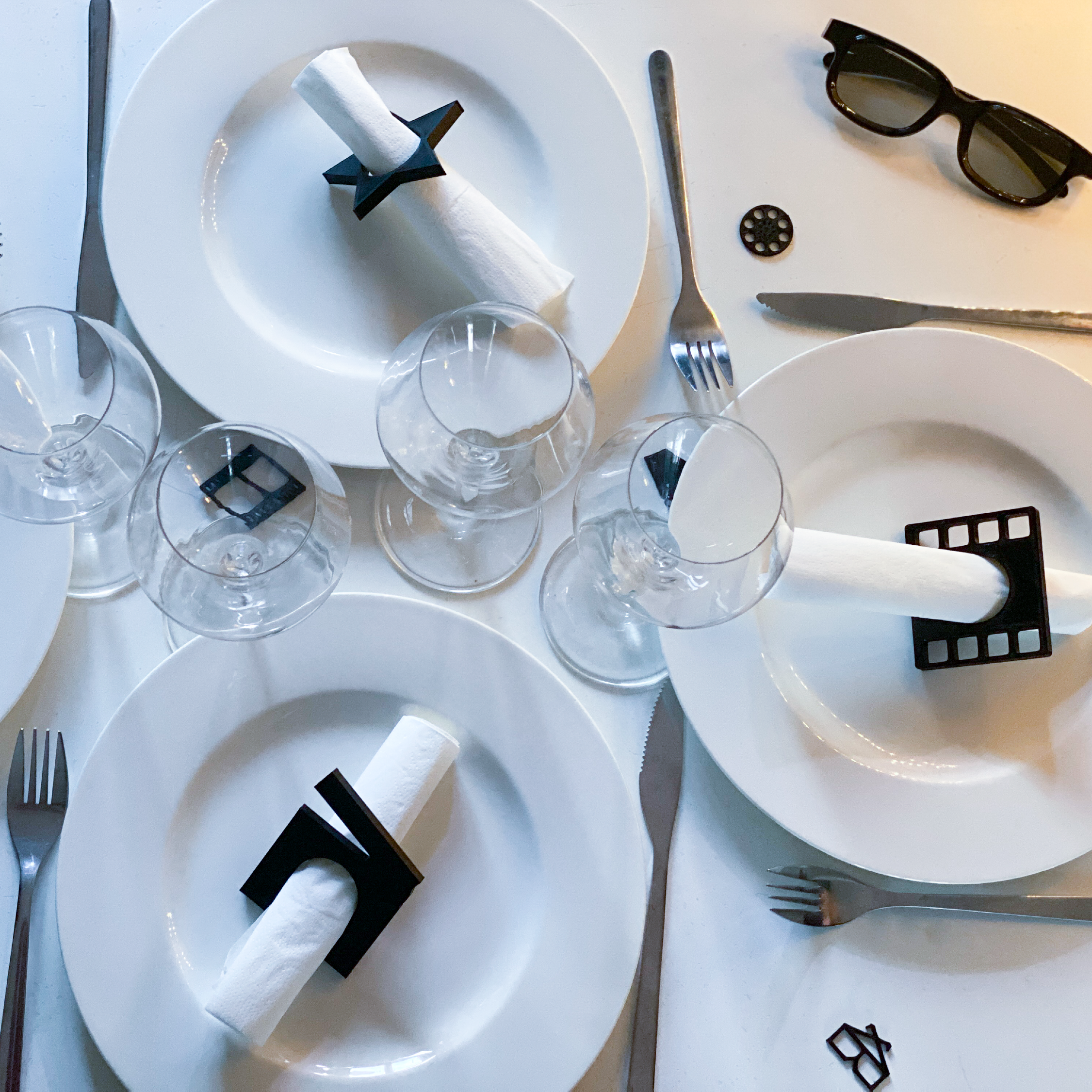 Ronds de serviette thème cinéma disposés sur une table blanche avec assiettes et verres, modèles étoile, clap, pellicule et bobine pour une décoration de fête stylée