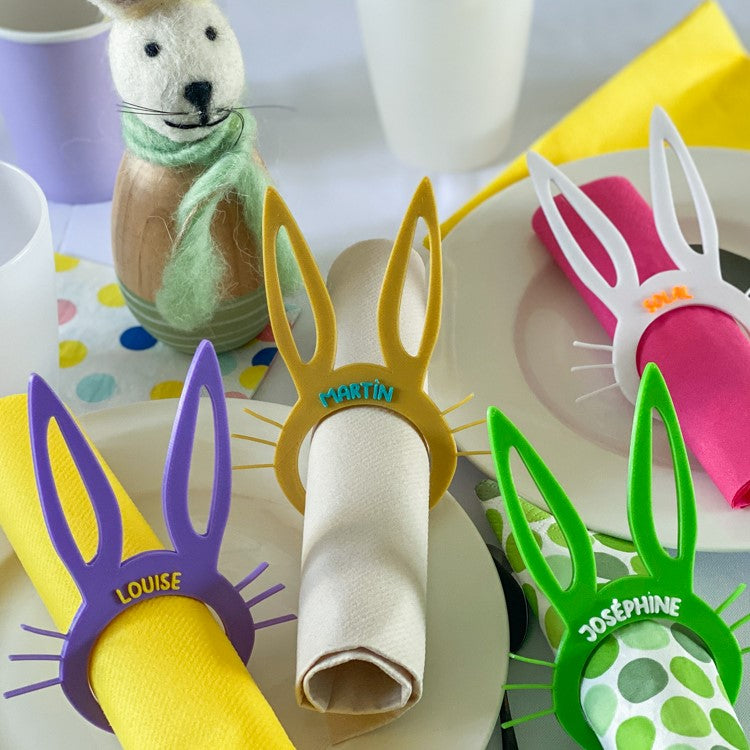 Ronds de serviette lapin personnalisés avec prénoms, utilisés comme marque-places pour une table de Pâques colorée.