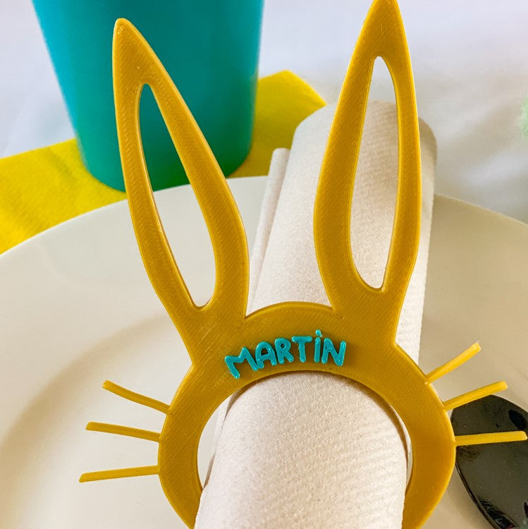 Rond de serviette lapin de Pâques miel personnalisé avec le prénom Martín, présenté autour d’une serviette roulée sur une table colorée.