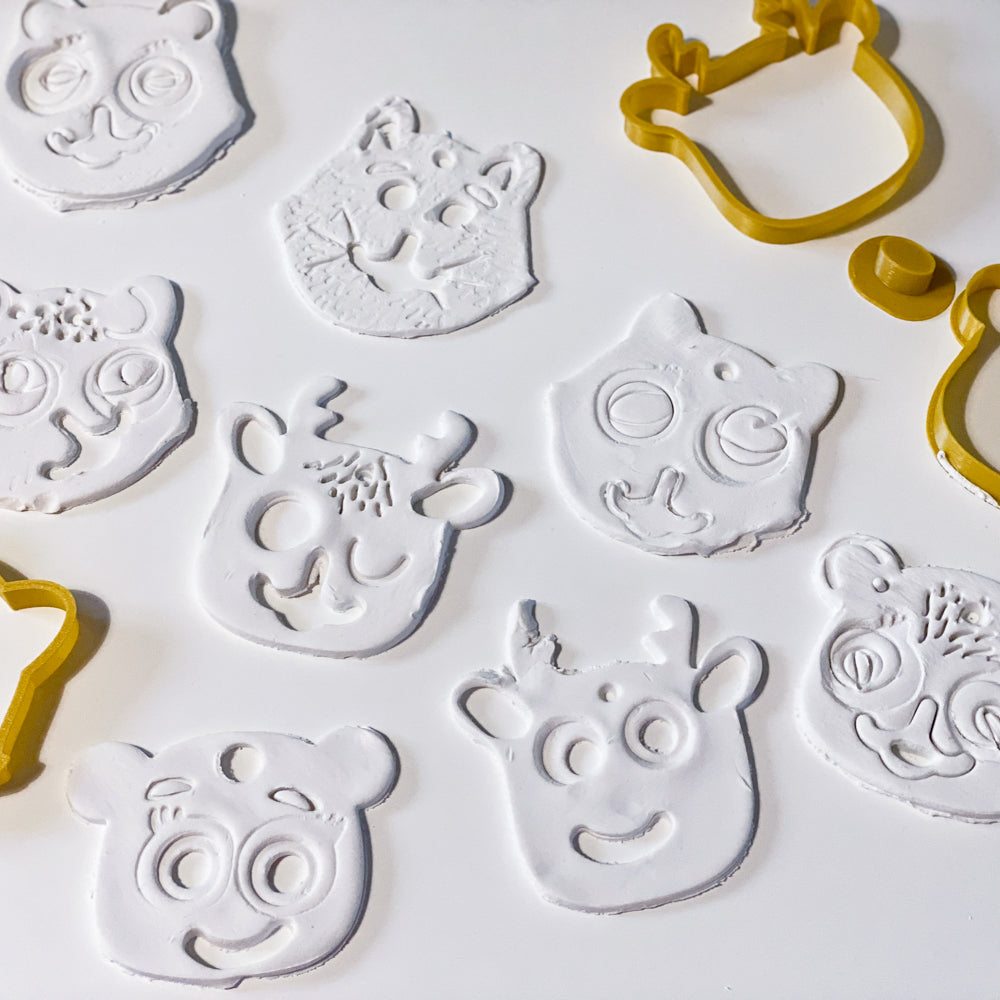 Image montrant plusieurs têtes d’animaux de Noël réalisées avec le kit emporte-pièces CililaCreation ; on voit différentes formes comme le renne, le raton laveur et l’ours, toutes découpées et texturées sur pâte blanche avec les emporte-pièces couleur miel.