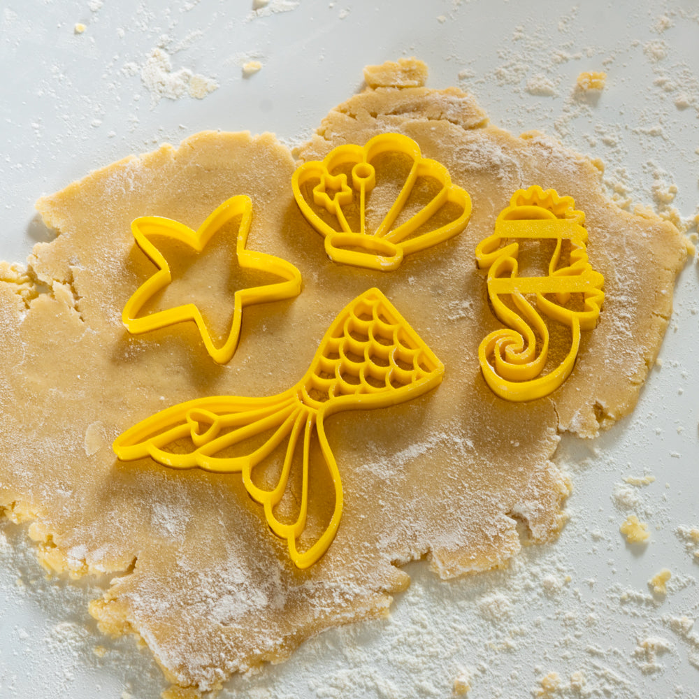 Empreintes d’emporte-pièces sirène avec queue de sirène, étoile de mer, coquillage et hippocampe dans une pâte sablée.